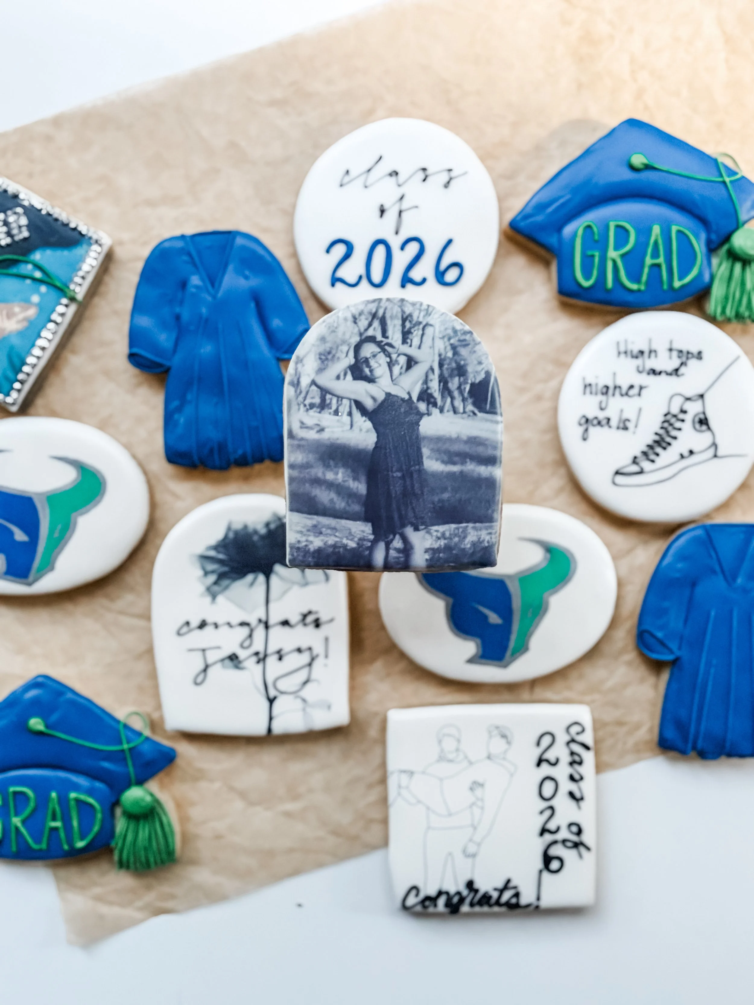 Assorted graduation-themed cookies, including ones shaped like graduation caps and featuring words like 'Grad' and 'Congrats', displayed on a surface.