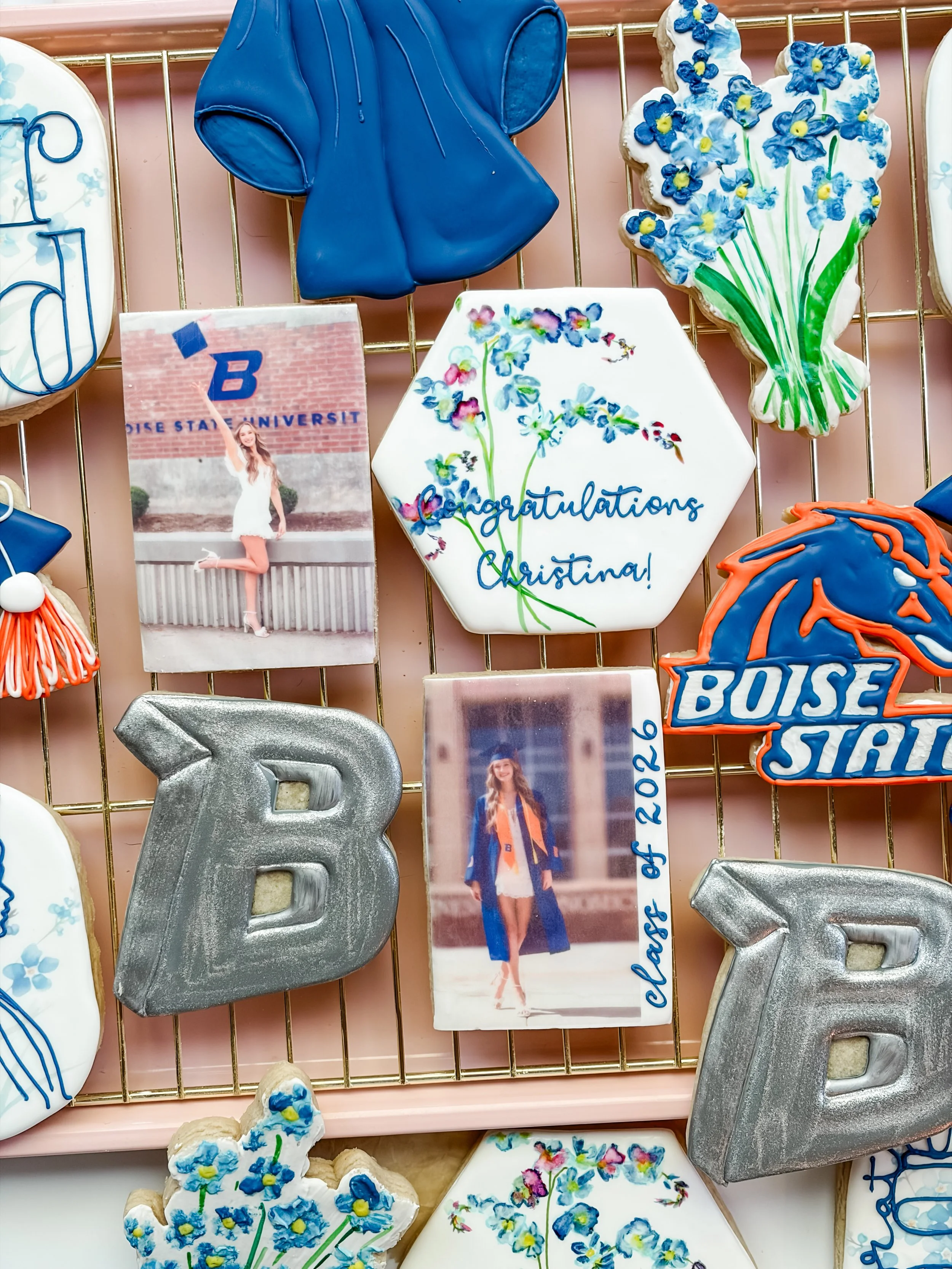 Decorative cookies and a photo of a graduate in cap and gown. The cookies include a blue mouse-shaped cookie, flowers, and a cheerleader cookie with the words "Congratulations Christina!".