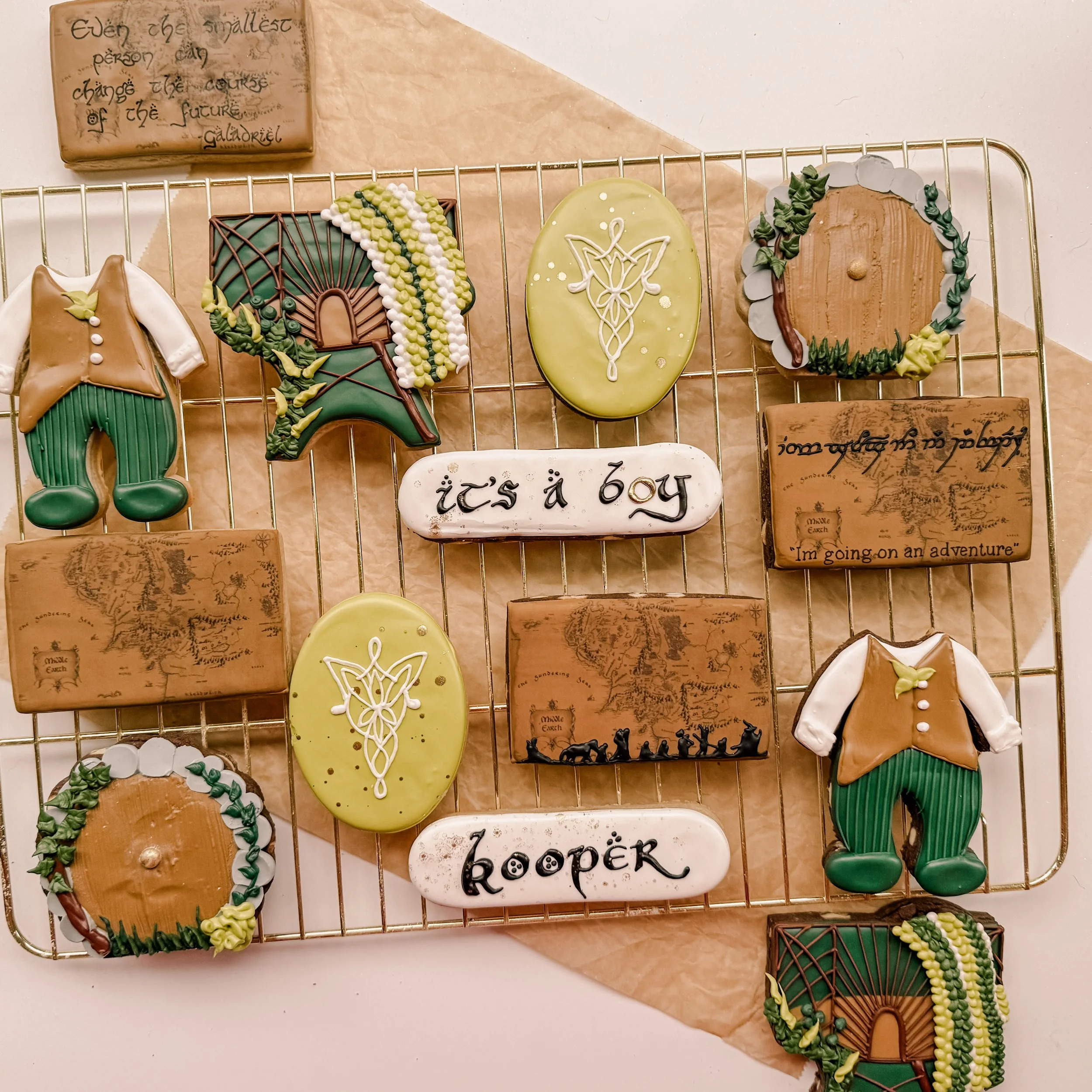 Decorative cookies on a wire rack, the mama-to-be requested a Lord of the Rings baby shower theme. Cookies are decorated with maps of Middle Earth, elvish symbols, and the fellowship of the ring walking.