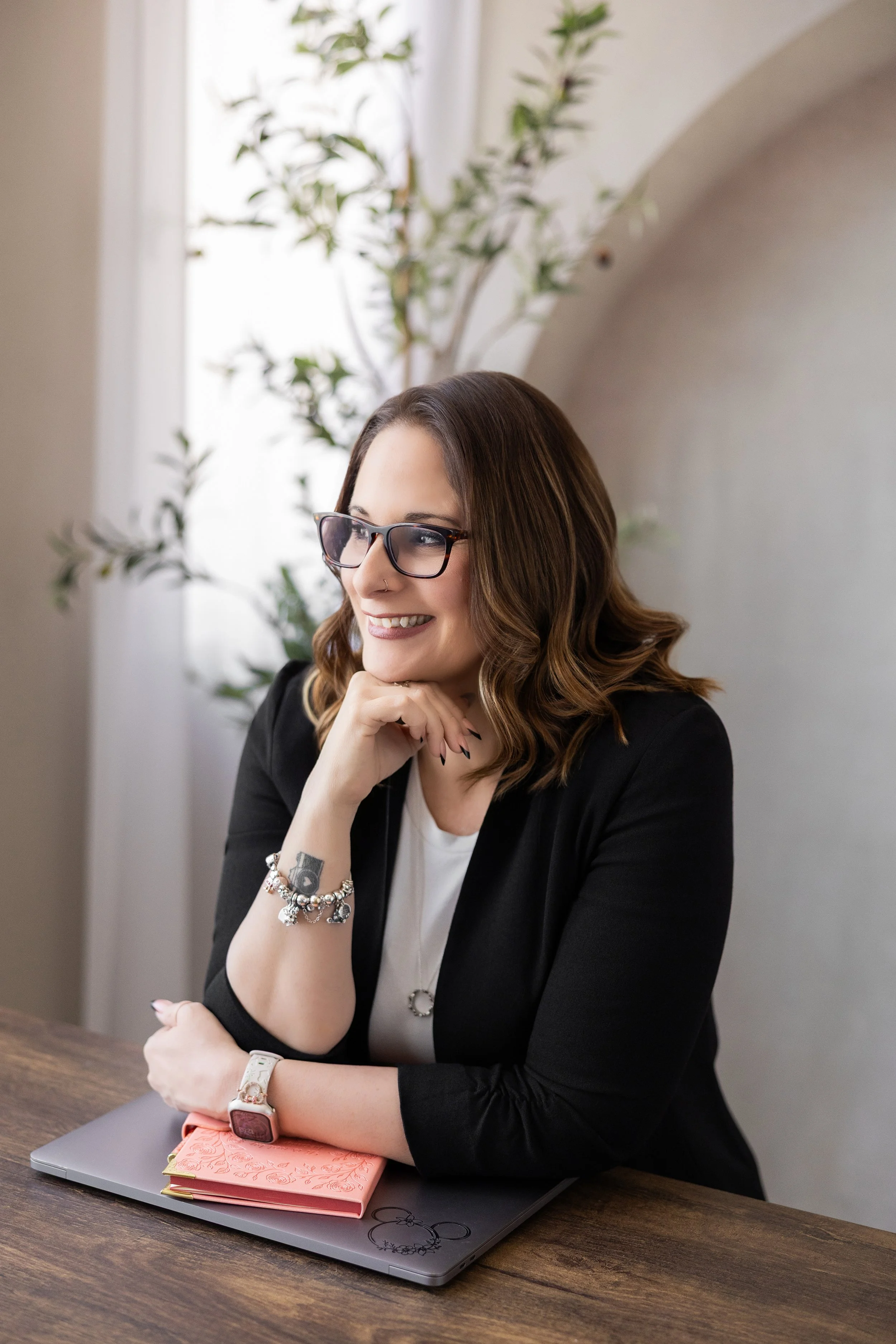Megan, small business operations and systems specialist sitting at a dark wood desk in natural light.
