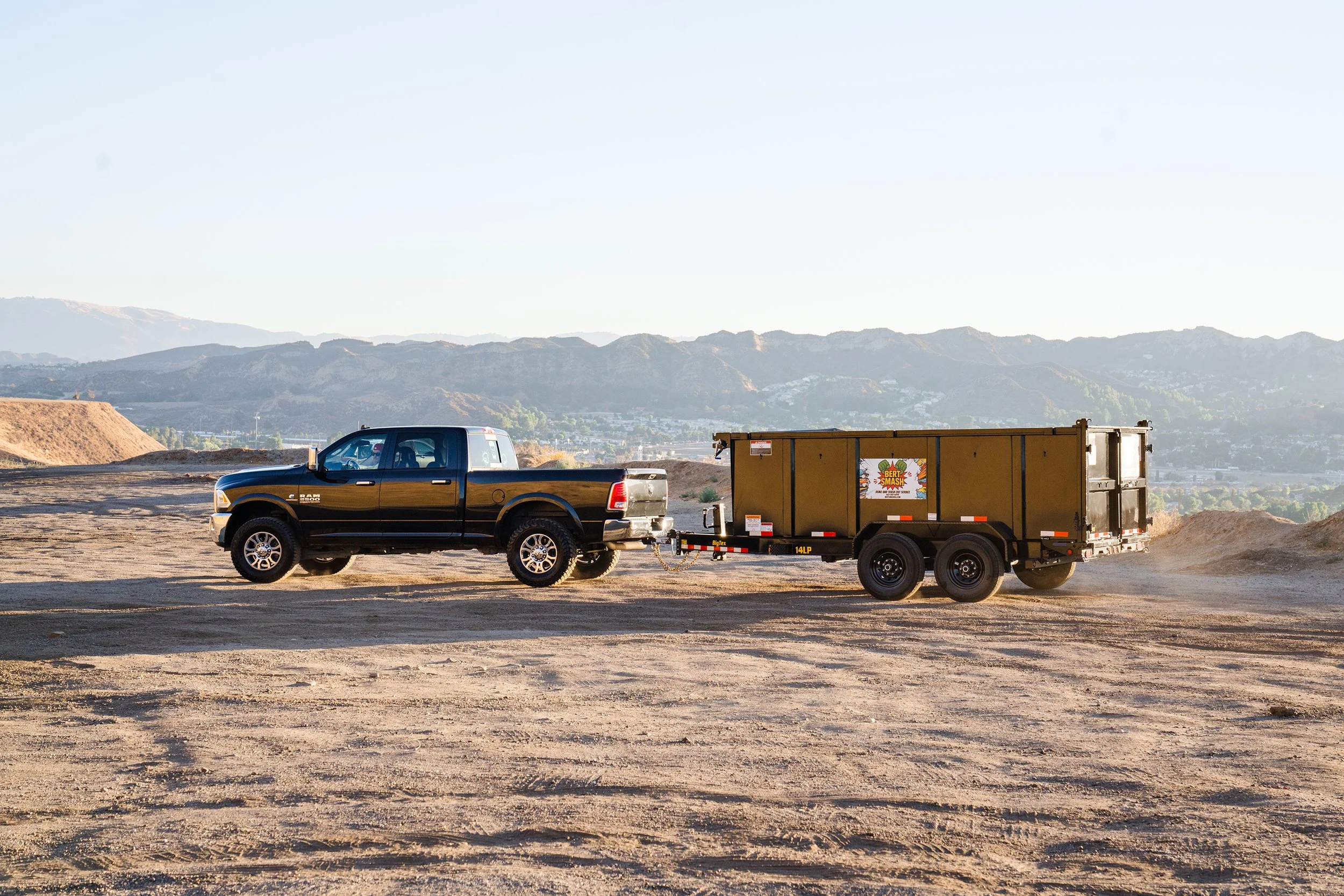 Black pickup truck towing a yellow garbage trailer on a dirt field with mountains in the background. Image taken by a Squarespace Website Designer for Small Business, The Simple Mouse.