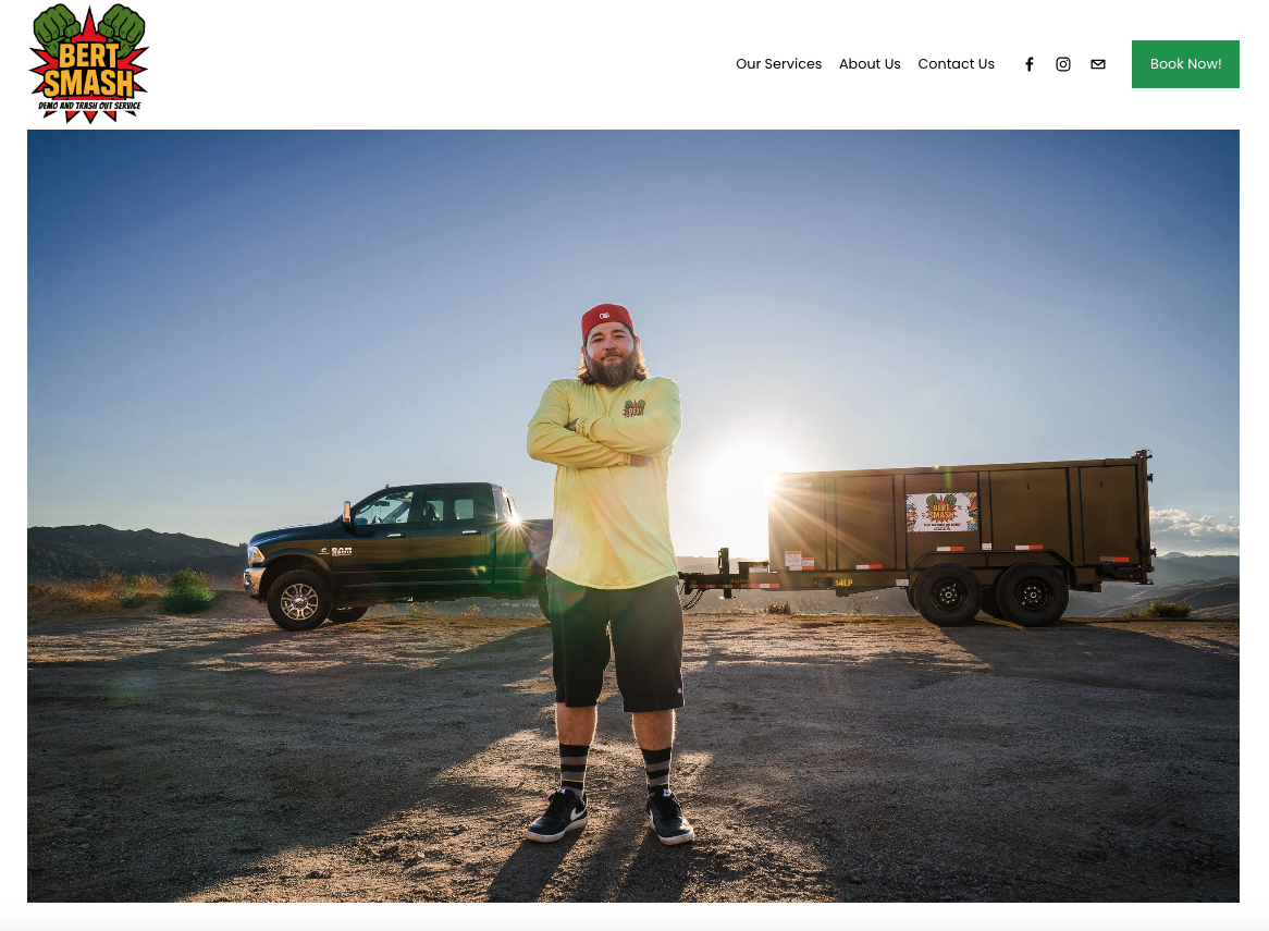 A website example of a small business launch with The Simple Mouse that shows aman with a beard, wearing a red hat and yellow long-sleeve shirt, standing with arms crossed in front of a flatbed truck and a black pickup truck on a dirt road at sunset.