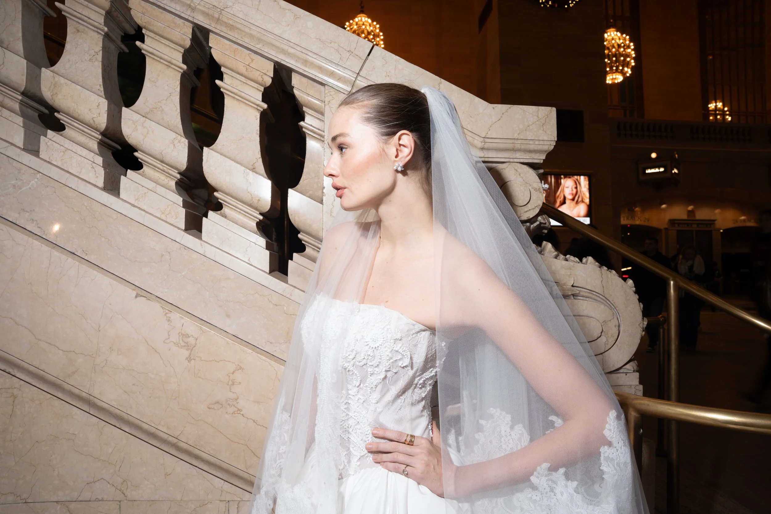Woman in wedding dress and veil posing on staircase inside building.