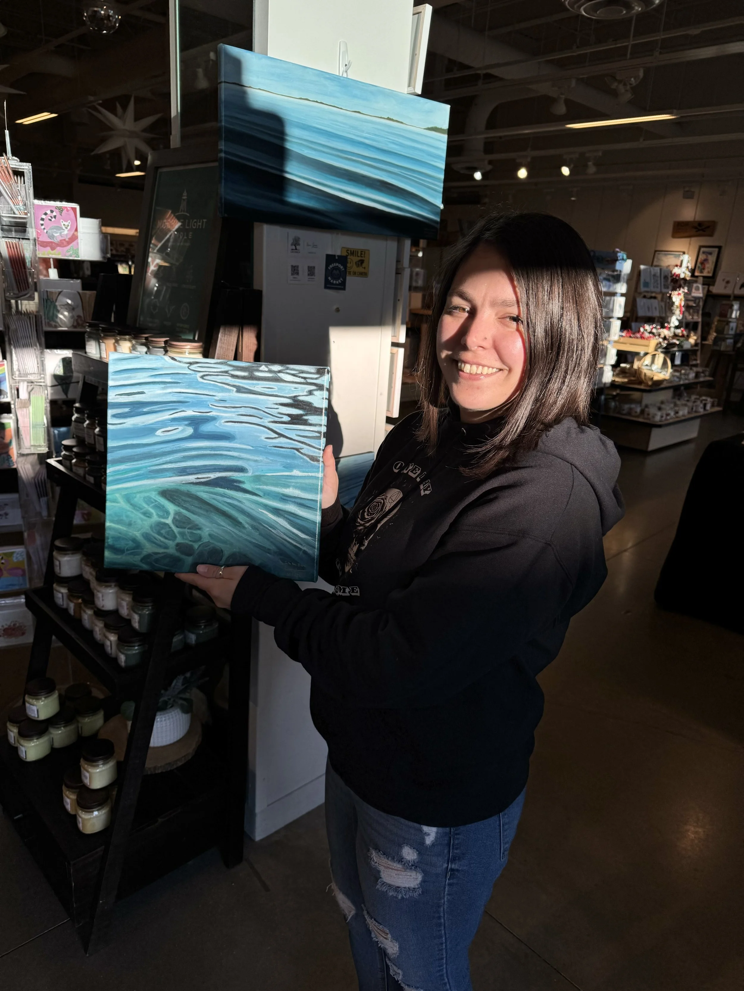 Maine Artist Sonia Jones inside a store holding her original painted canvas of the surface of water