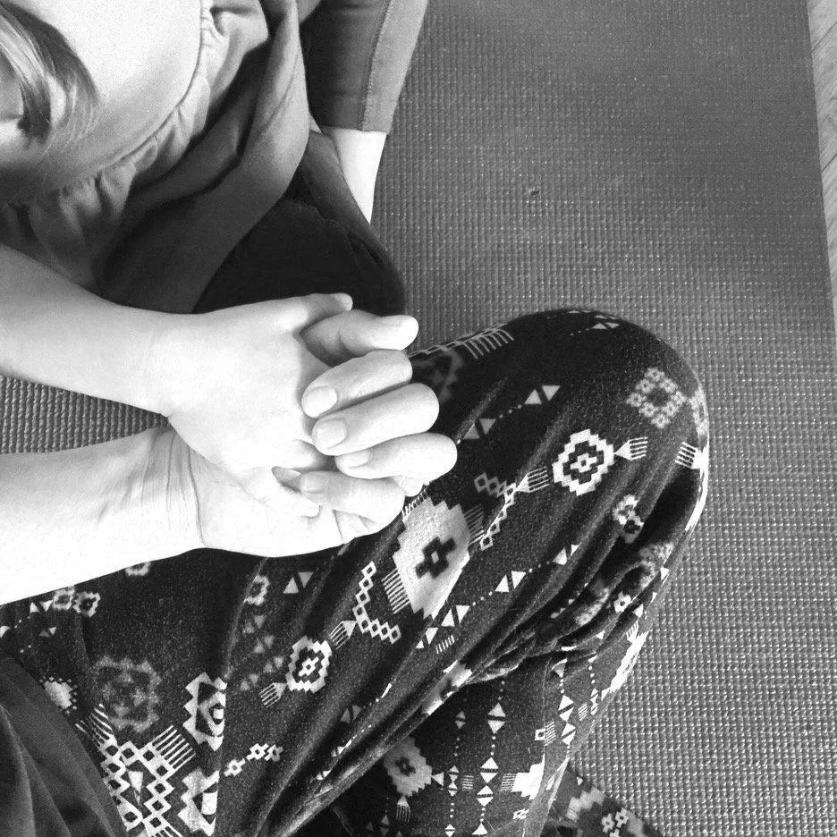 A person and a child holding hands, sitting on a textured floor mat. The person's arm and hand are visible, with the child sitting beside them.