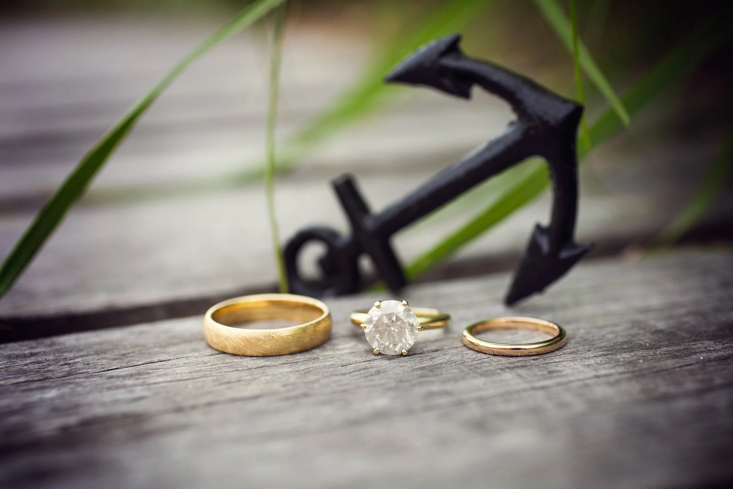 Three rings and an anchor-shaped ornament on a wooden surface, with green grass blades and out-of-focus background.