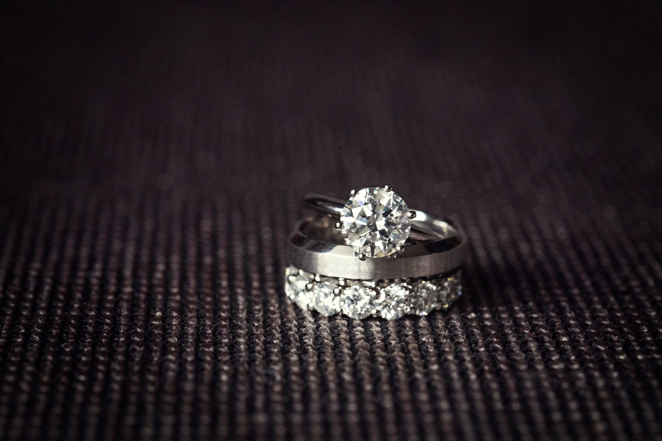 A diamond engagement ring and a diamond wedding band resting on a textured purple surface.