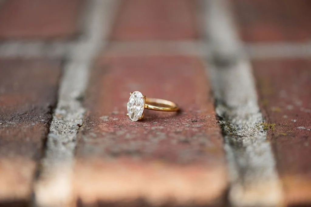 A gold ring with a large oval diamond, lying on a weathered brick pavement.