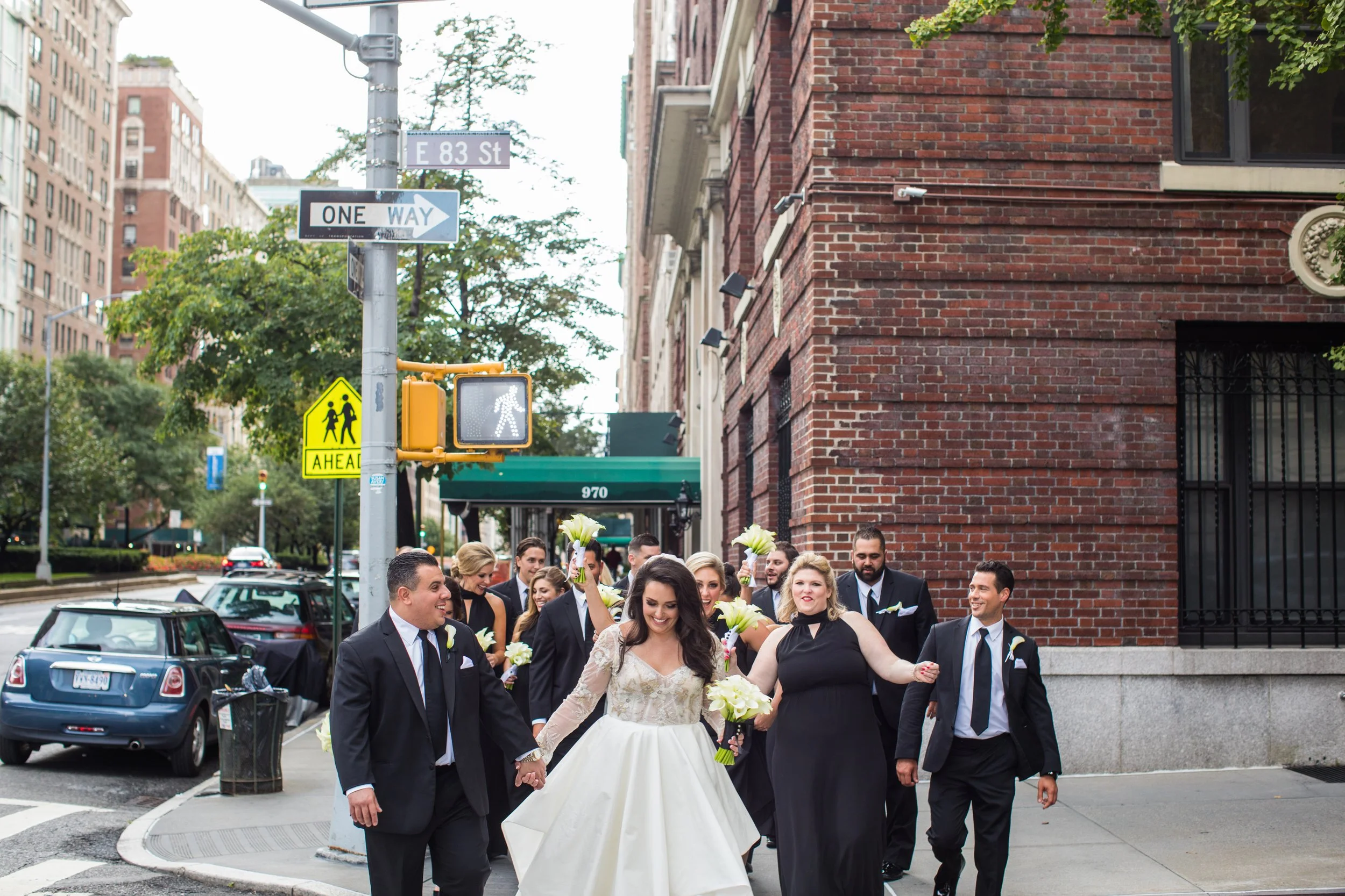 A bride and groom walking hand in hand with friends on a city street corner.
