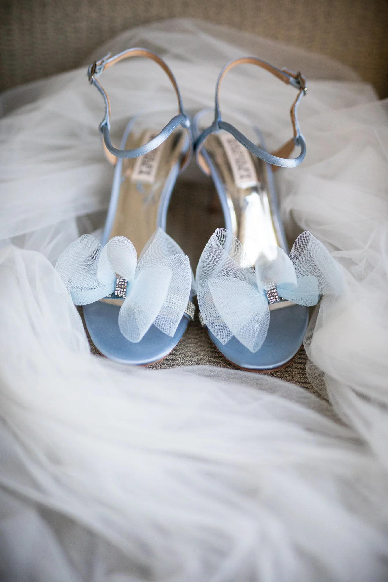 Light blue high heel shoes with bows and rhinestones, surrounded by white tulle fabric.