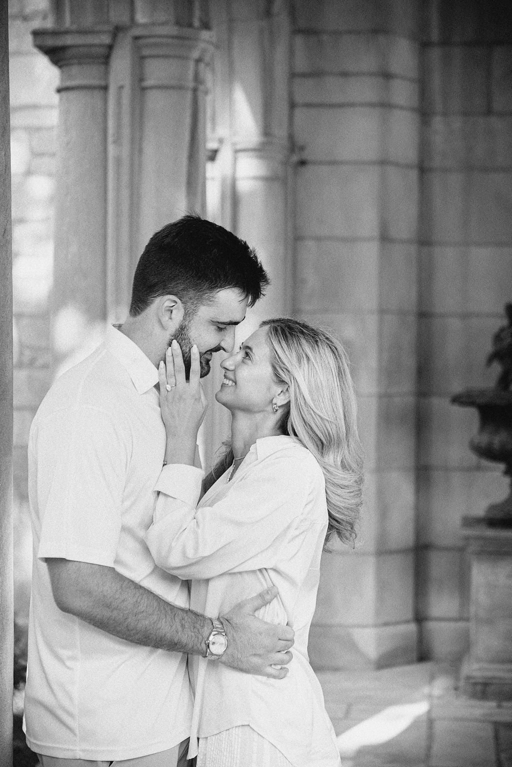 A couple in an affectionate moment indoors, with the woman touching the man's face, both smiling and looking into each other's eyes.
