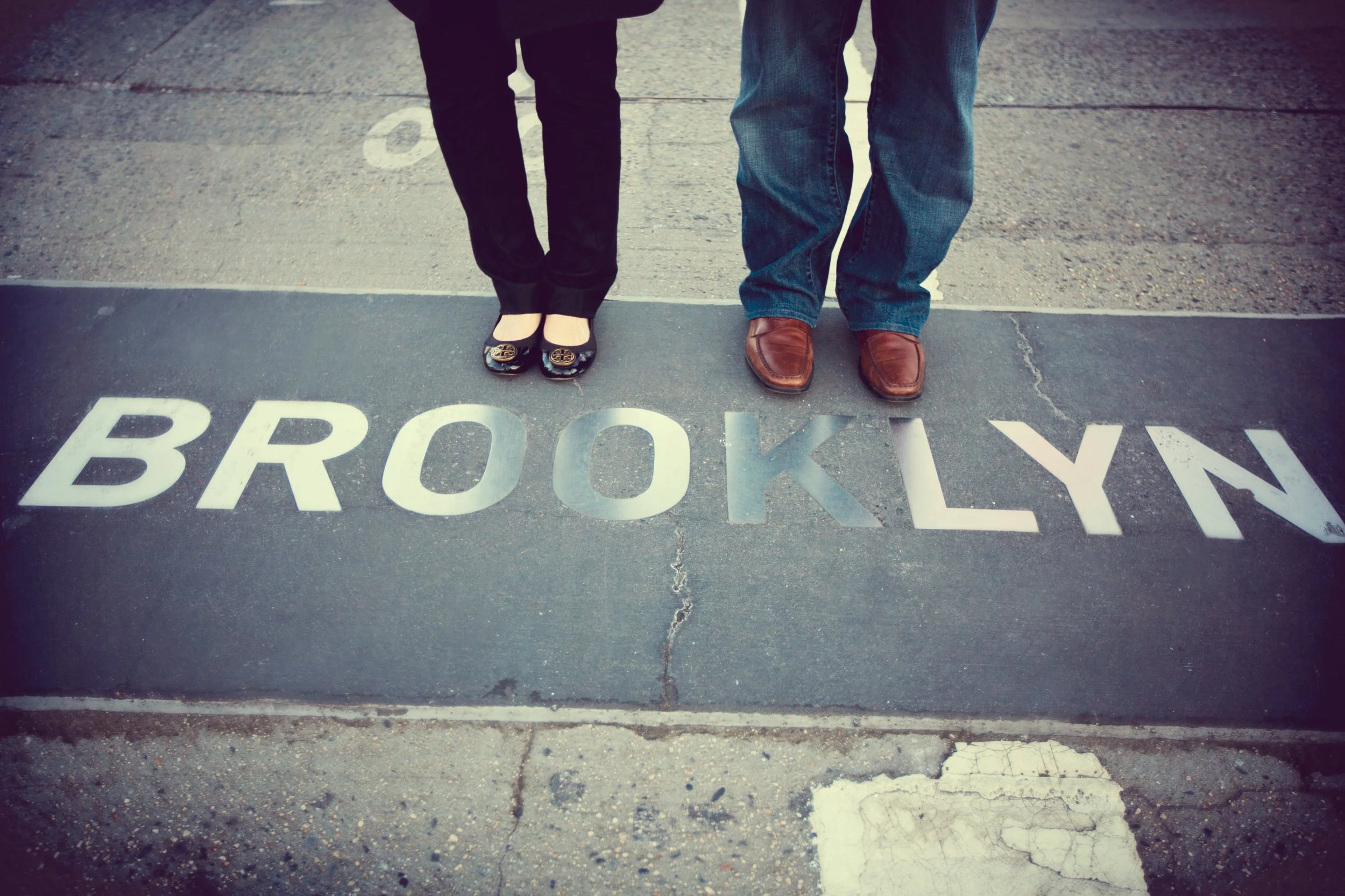 People standing on a sidewalk next to a street sign that reads 'BROOKLYN'.