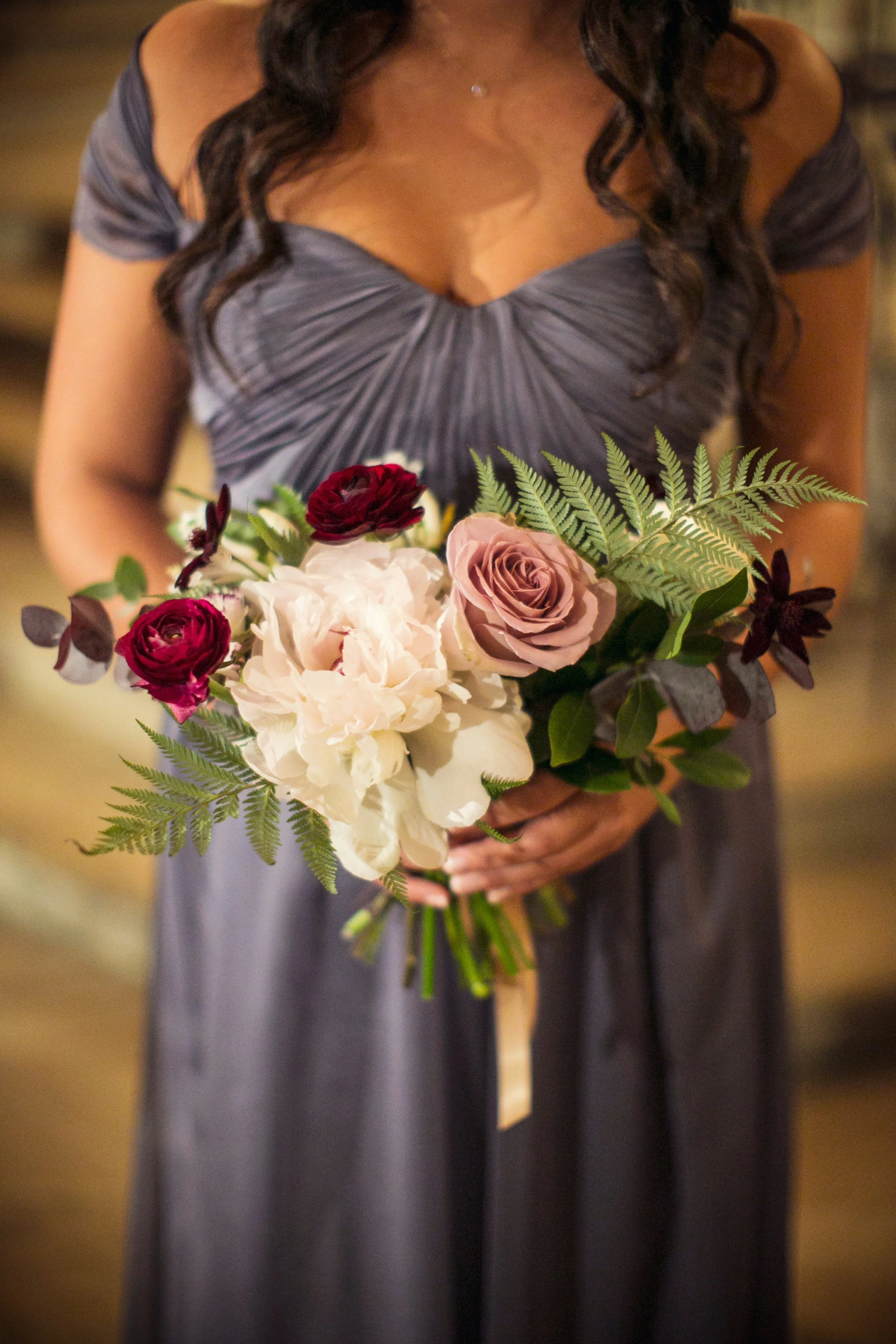 A woman in a gray dress holding a bouquet of flowers featuring white, pink, and red blooms with green and dark purple leaves.