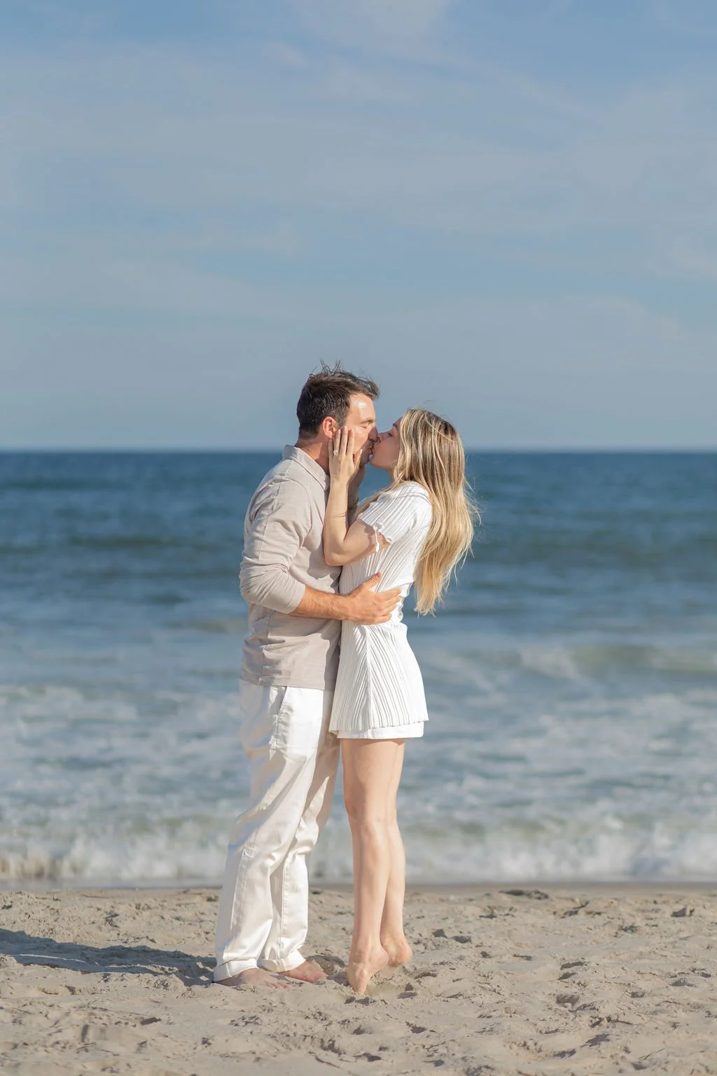 A couple in white clothes kissing on a beach.