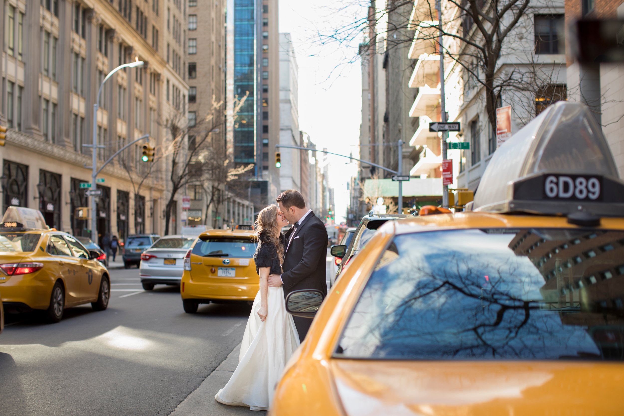A couple sharing a kiss on a city street surrounded by yellow taxis and tall buildings.