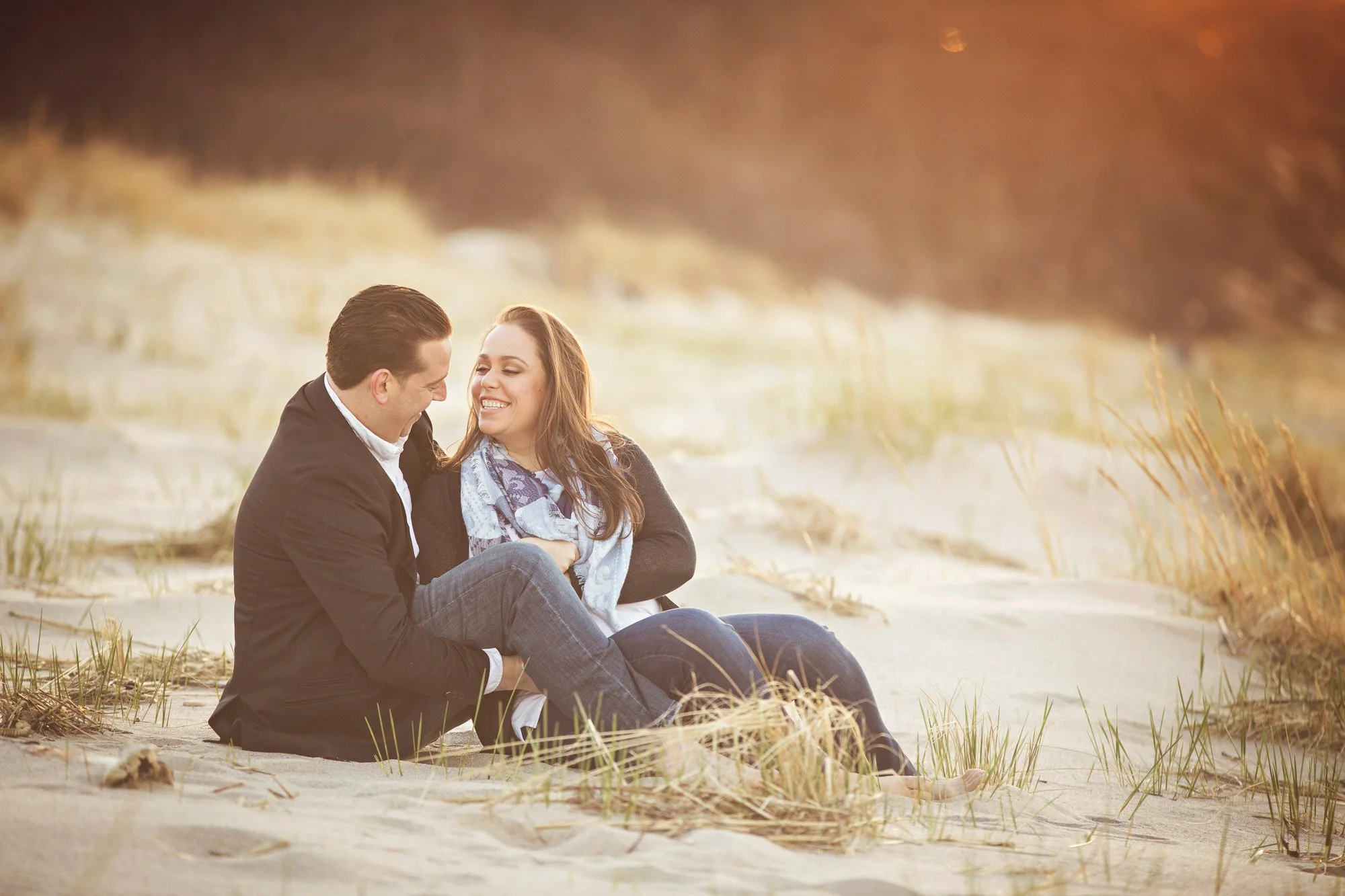 A couple sitting on the sand at the beach, smiling and enjoying each other's company during sunset.