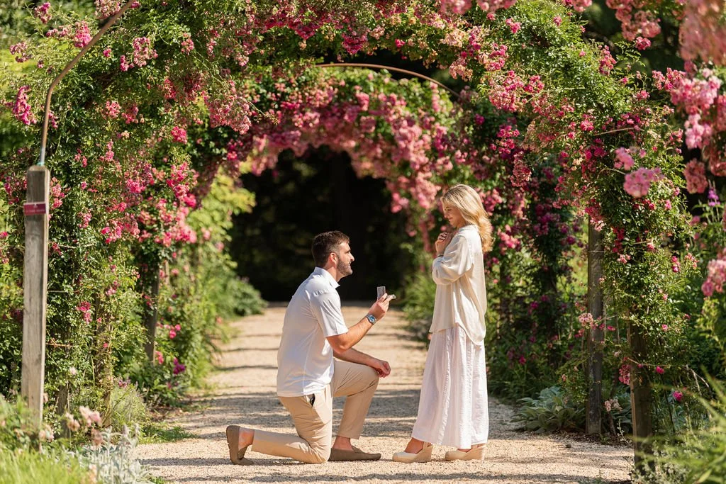 A man proposes marriage to a woman in a garden with pink and purple flowers