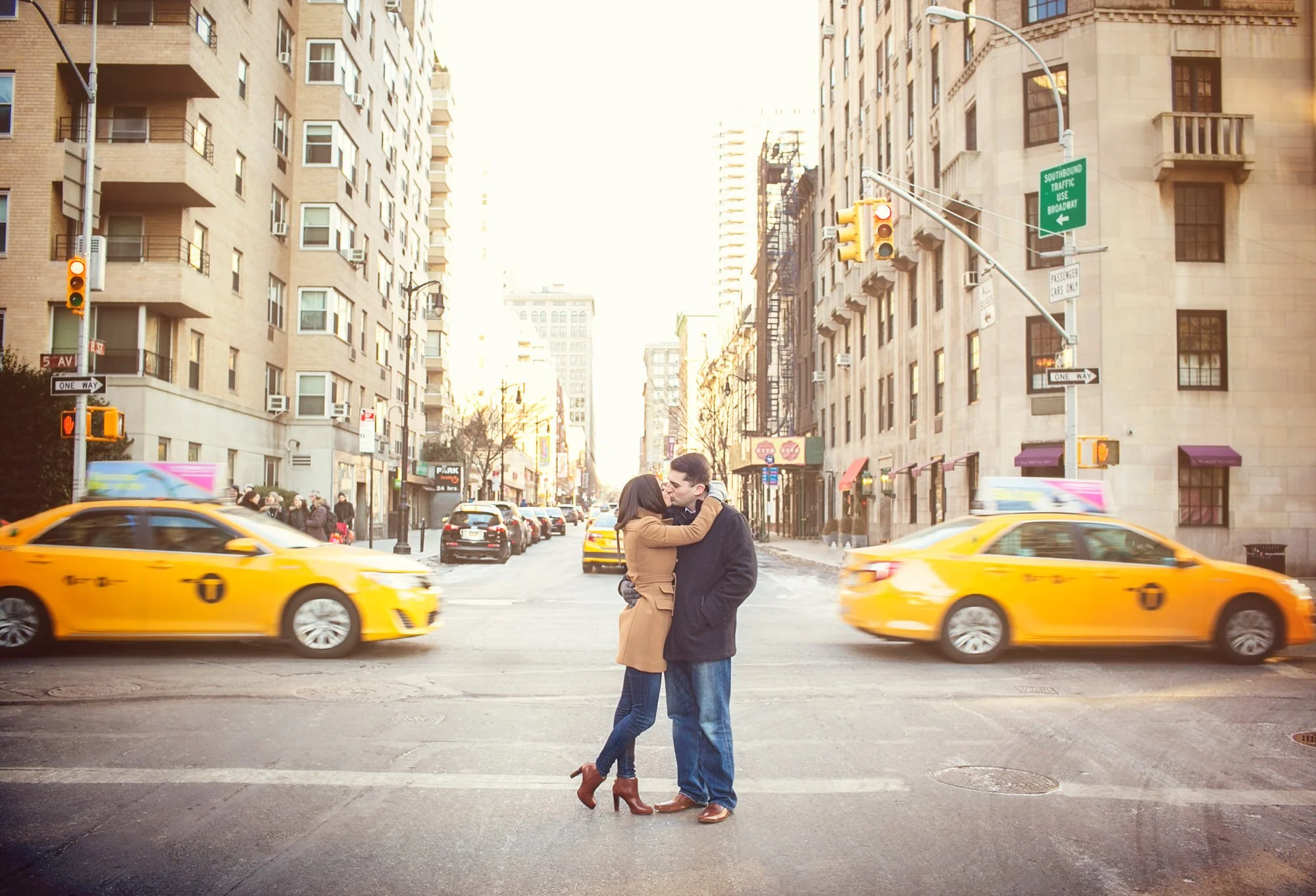 A couple embracing and kissing in the middle of a city street with yellow taxis and tall buildings.
