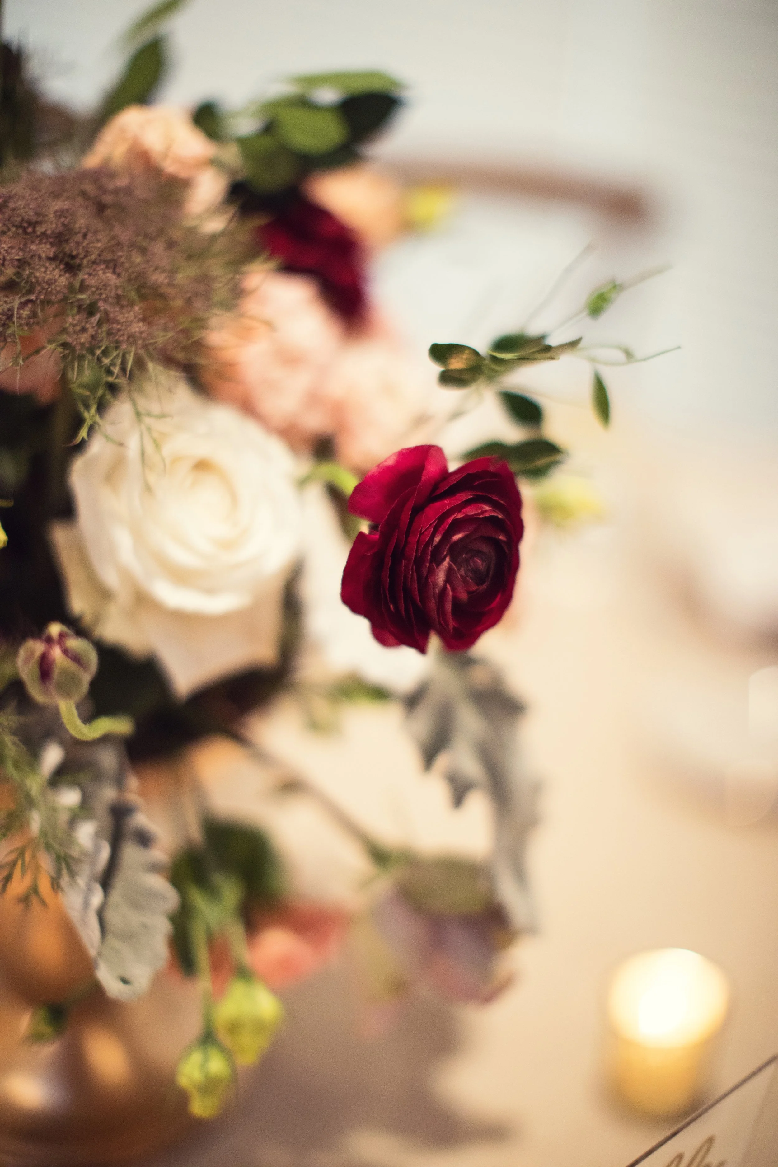 Close-up of a burgundy rose in a floral arrangement with white and pink flowers and greenery.