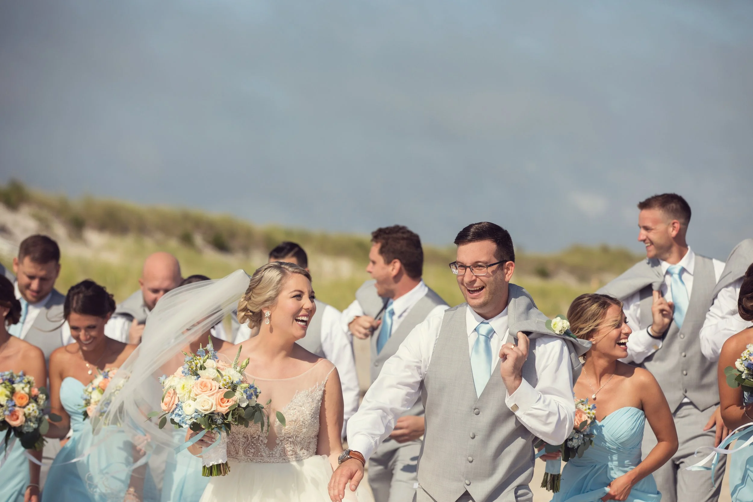 Happy wedding party outdoors with the bride, groom, bridesmaids, and groomsmen, smiling and celebrating on a sunny day.