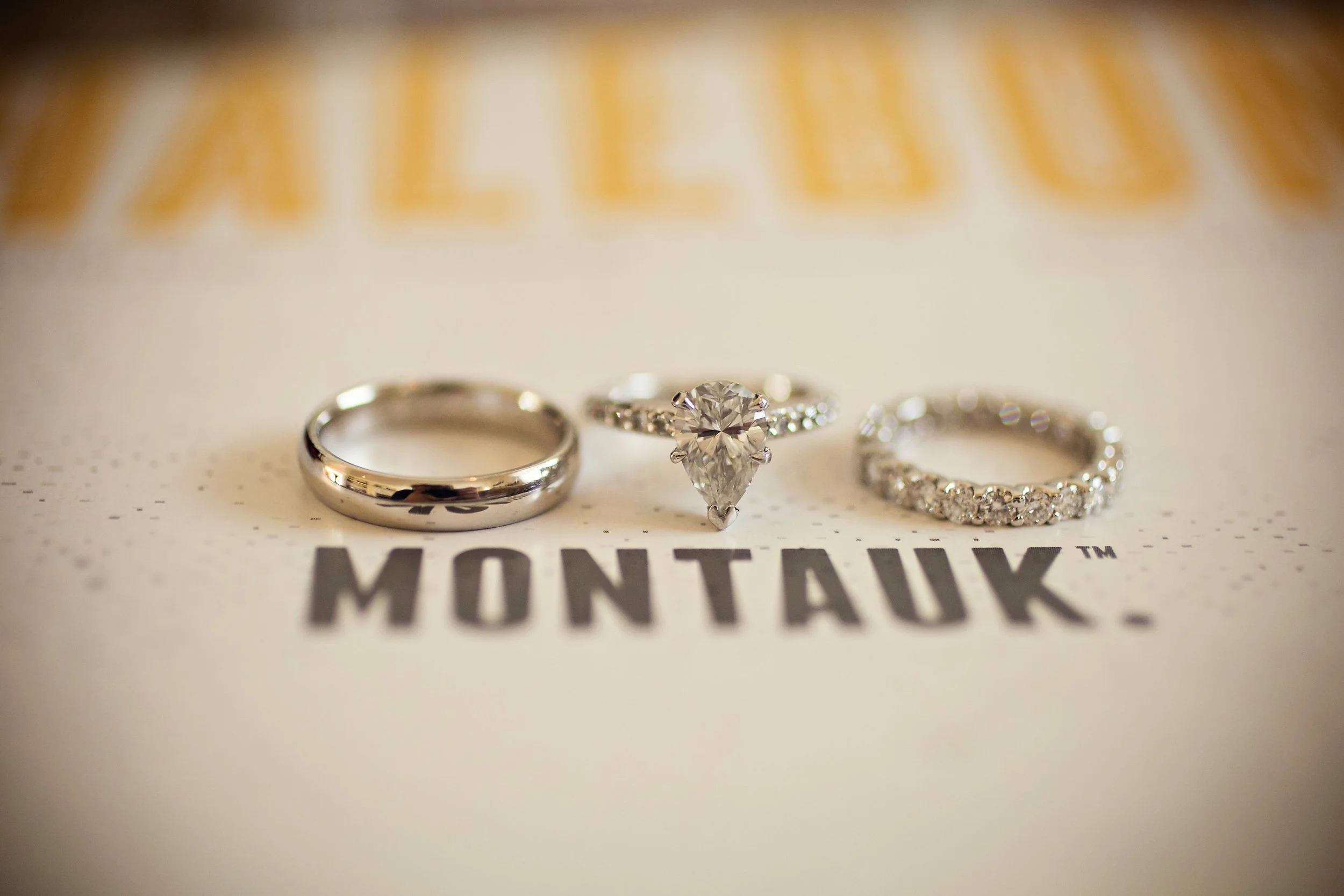 Three rings—two diamond engagement rings and one wedding band—placed on a Montauk branded surface.