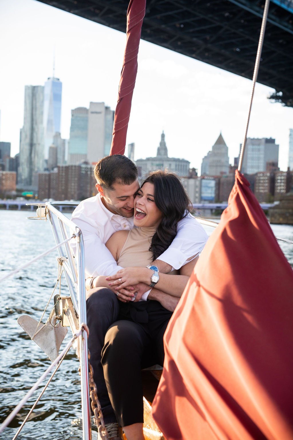 A happy couple hugging and smiling on a boat with a city skyline in the background.