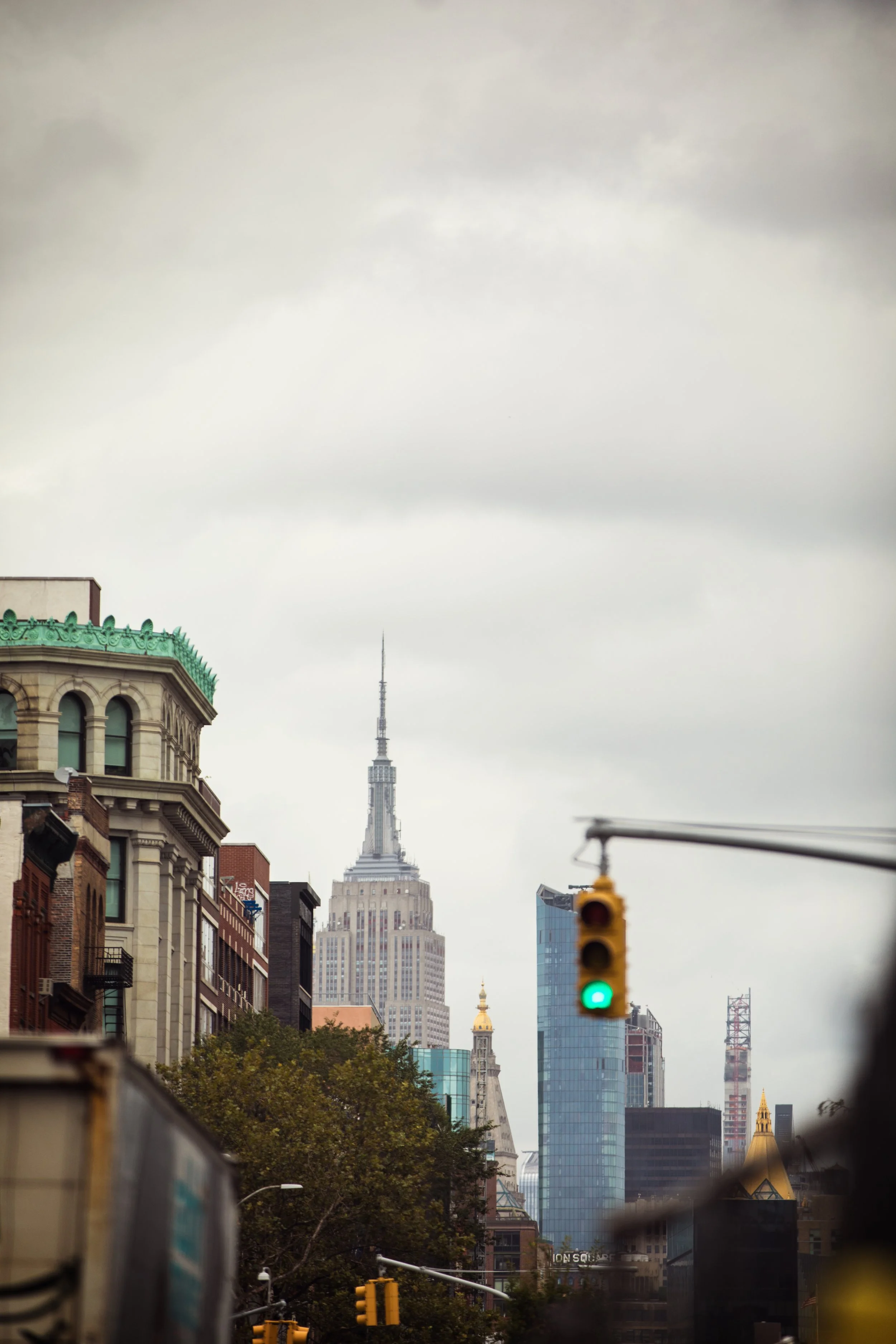 Cityscape of New York City with Empire State Building and traffic light showing green on a cloudy day.