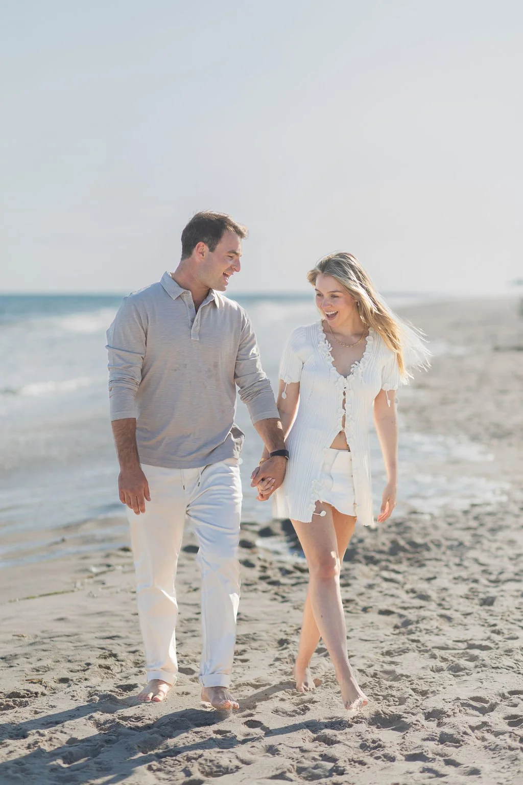 A couple walking hand-in-hand on a sandy beach, smiling and enjoying each other's company.