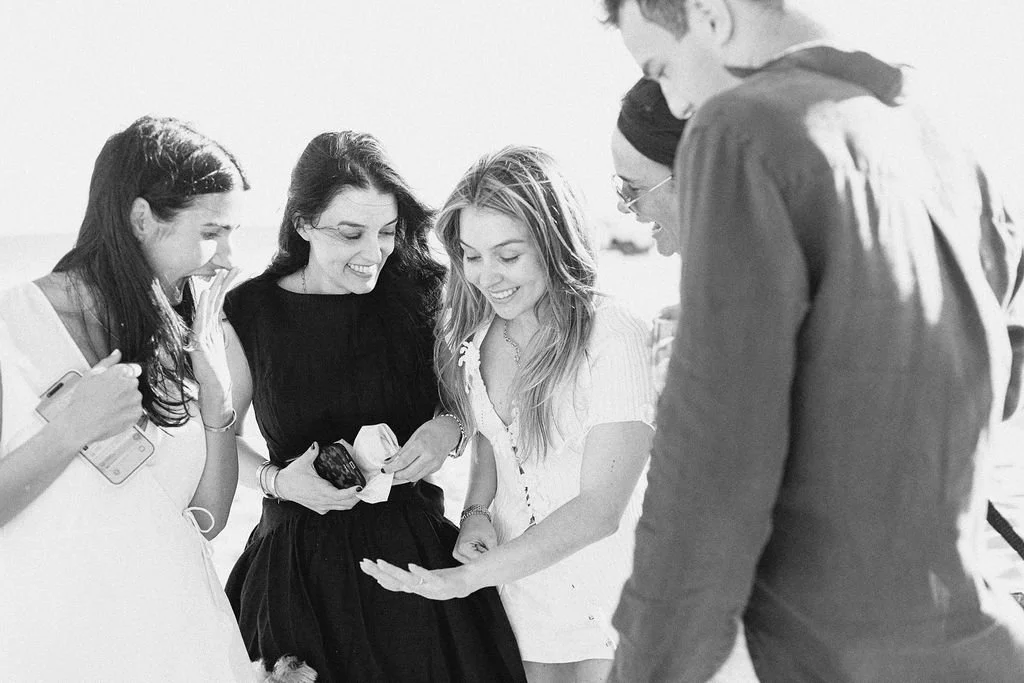 Group of five young adults standing outdoors, looking at a woman's hand with smiles.