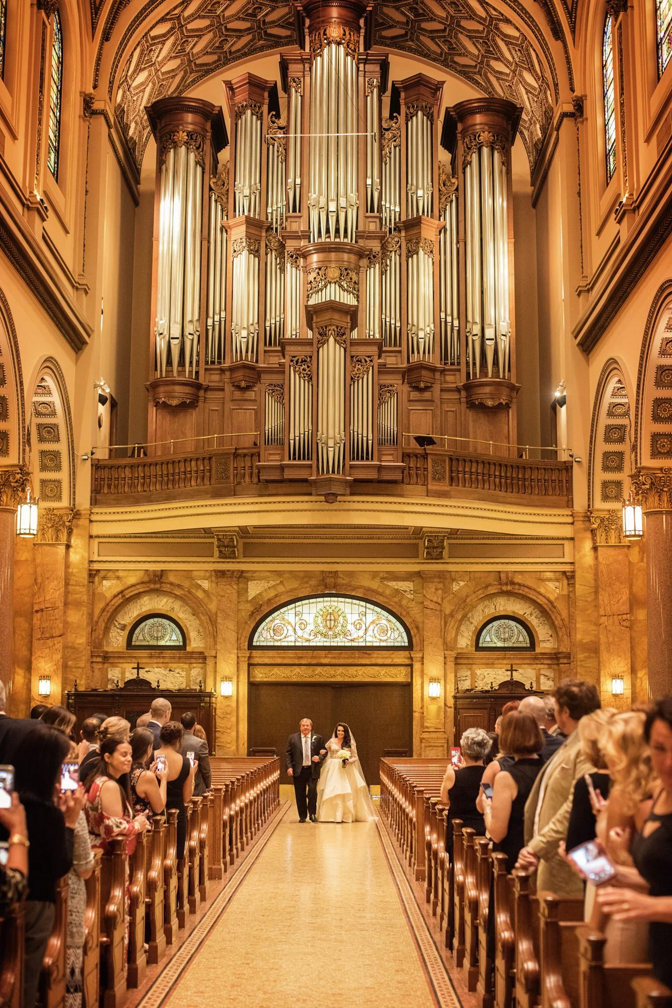A bride walking down the aisle at a wedding ceremony inside a grand, ornate church with a large pipe organ in the background.