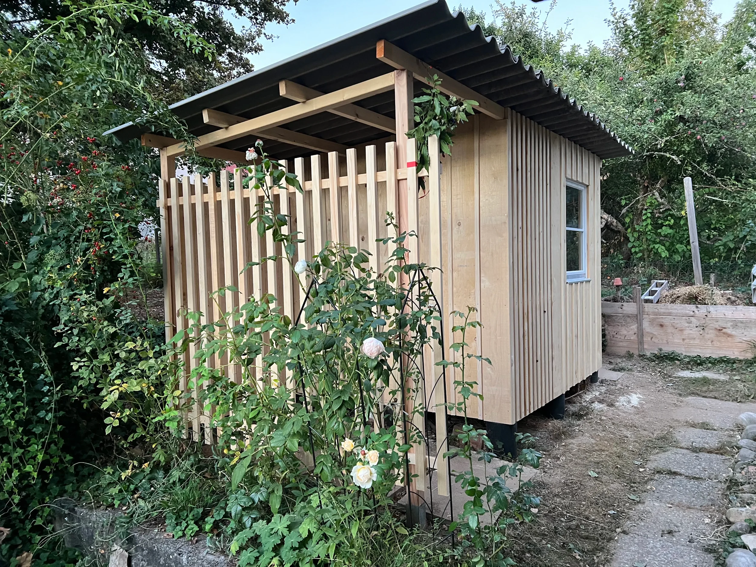 Ein Holzhaus im Garten, umgeben von Büschen und Bäumen.