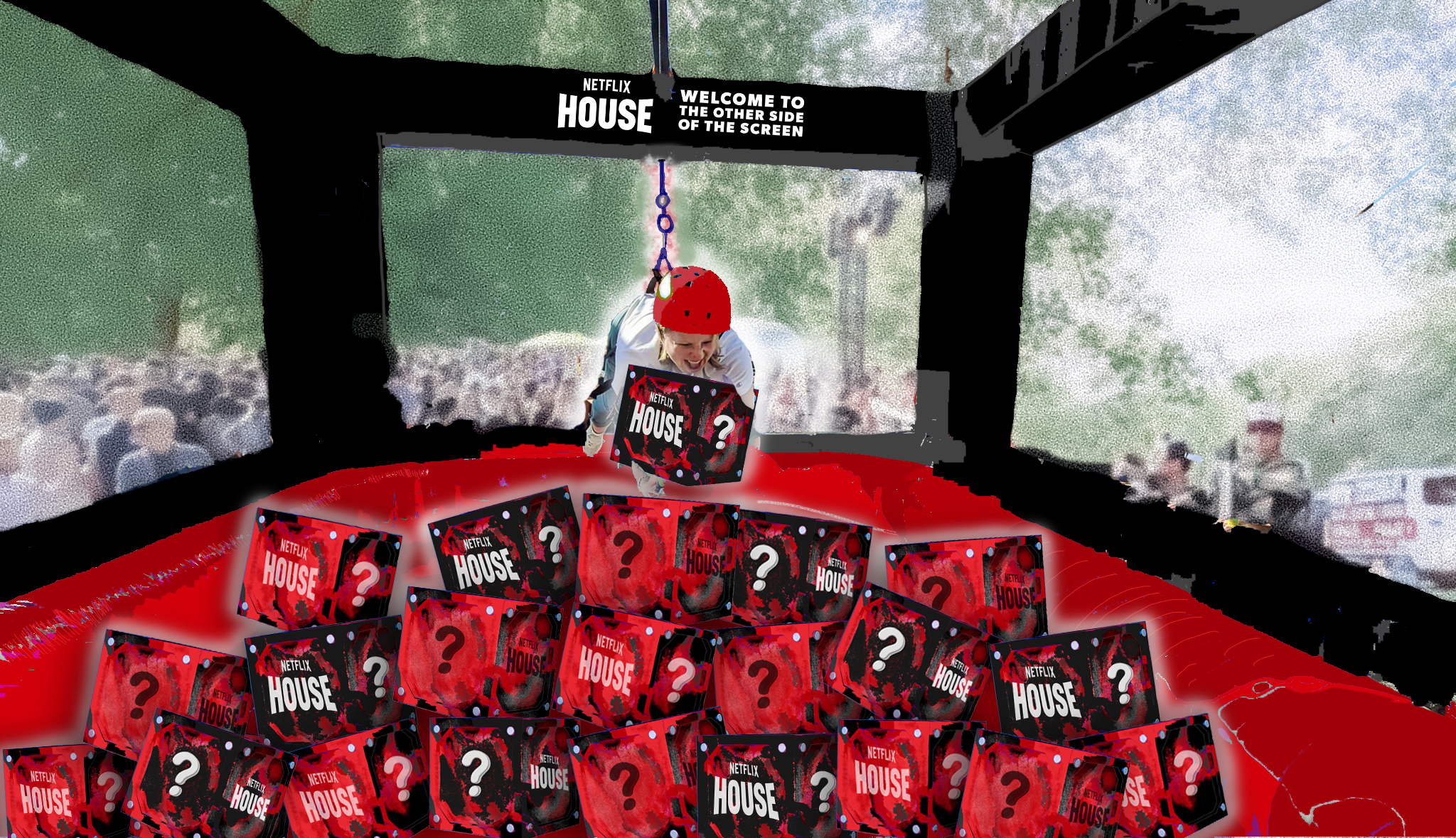 A person wearing a helmet is inside a life-size prize machine wit a box with the Netflix House logo. Several similar logos are on boxes piled on the floor. The background shows a crowd and outdoor scenery with trees, seen through large glass windows.