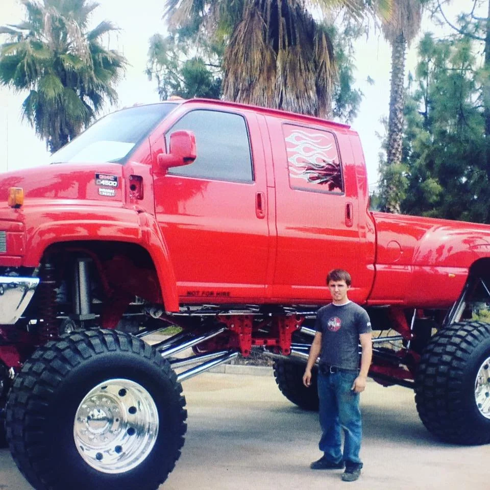 A young Matthew Johnson (Johnson Motorsports Owner) standing next to an oversized red pickup truck with large off-road tires and suspension.
