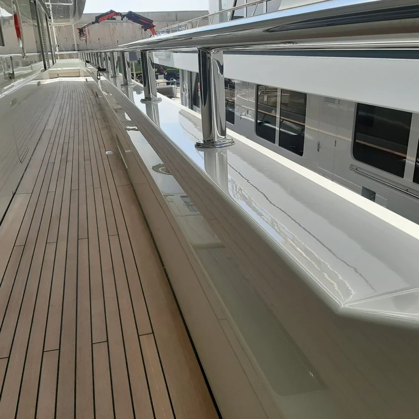 Close-up view of a yacht deck showing polished metal railings, wooden decking, and a boat docked nearby.