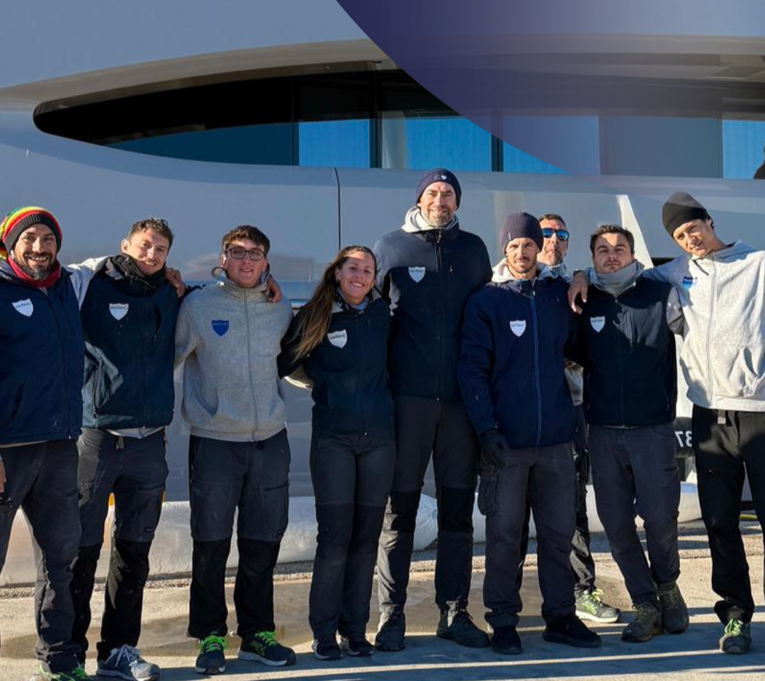 Group of nine people standing outdoors in front of a modern building, dressed in athletic and winter clothing, smiling.