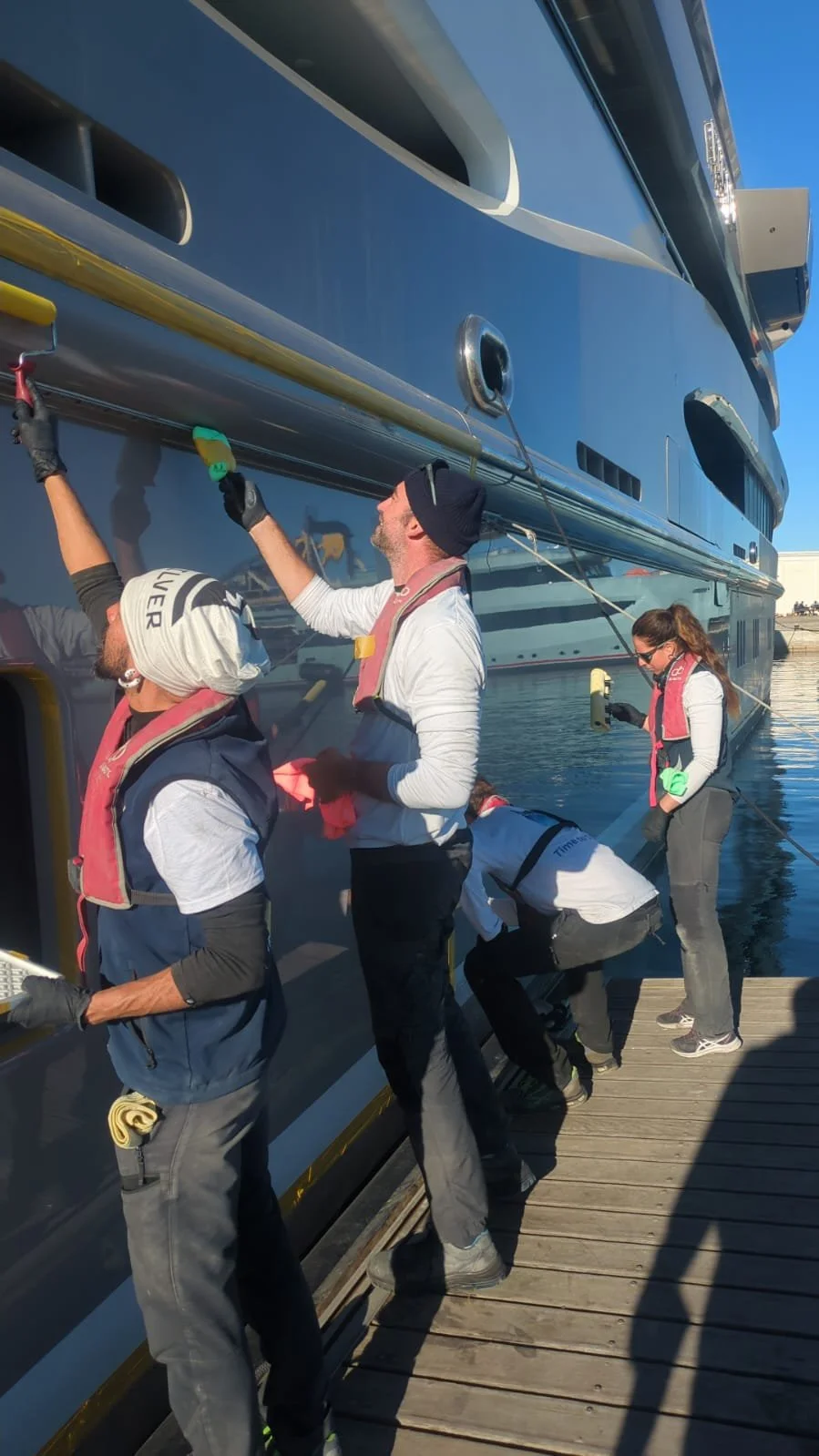 People working on a large boat docked at a pier, painting and performing maintenance.