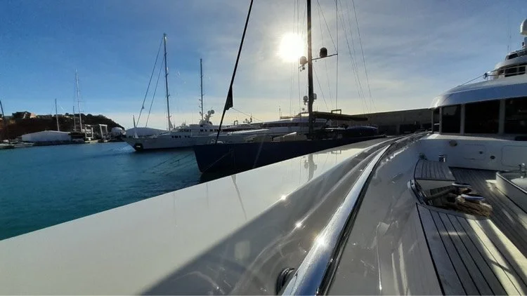 View from a yacht showing other sailboats and yachts docked at a marina with the sun in the sky.