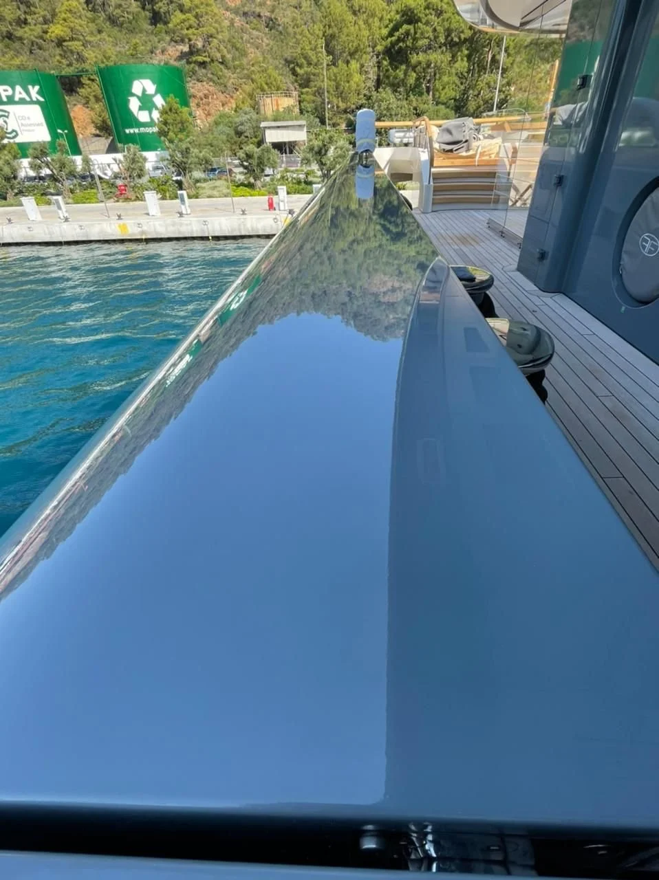 Reflection of trees and sky on the shiny surface of a boat's side at a dock.