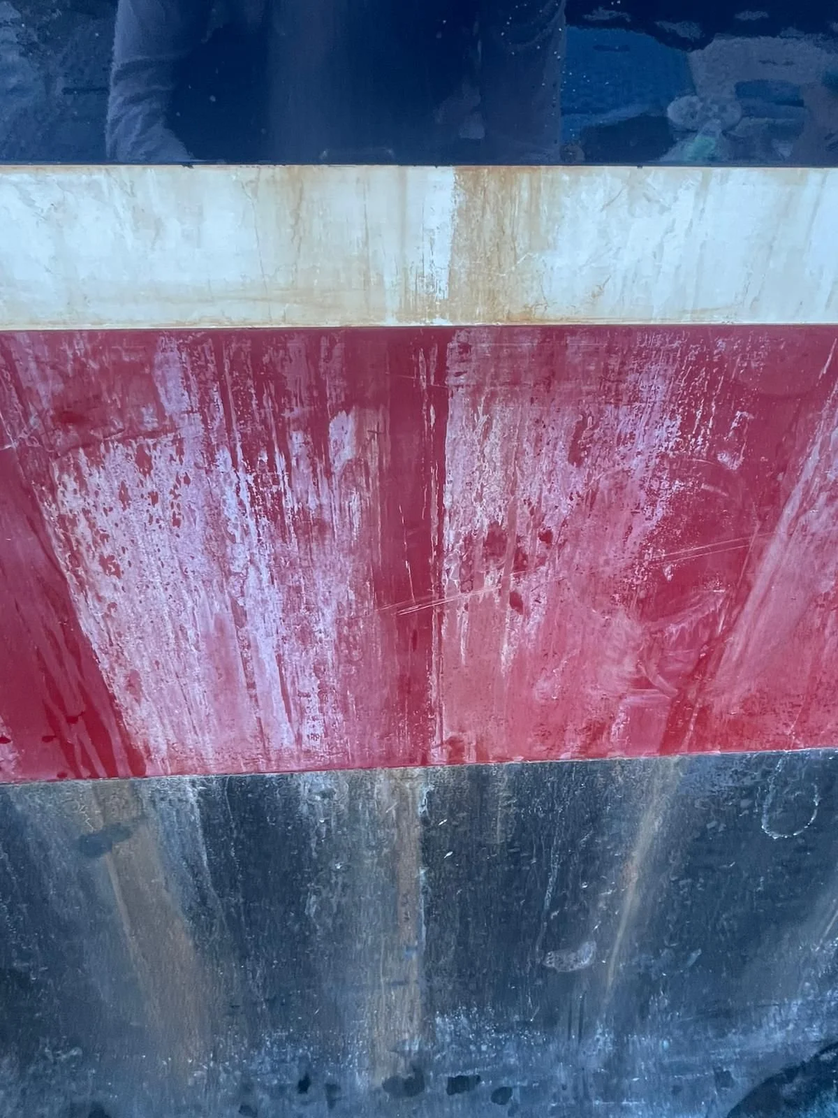 Close-up of a metallic surface with horizontal color bands: black at the top, beige in the middle, red below, and blue at the bottom, with visible scuffs and scratches.