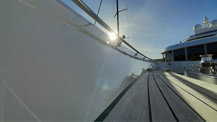 Looking down a yacht dock, with the sun shining on the side of the vessel, featuring a wooden deck and adjacent parts of other yachts.