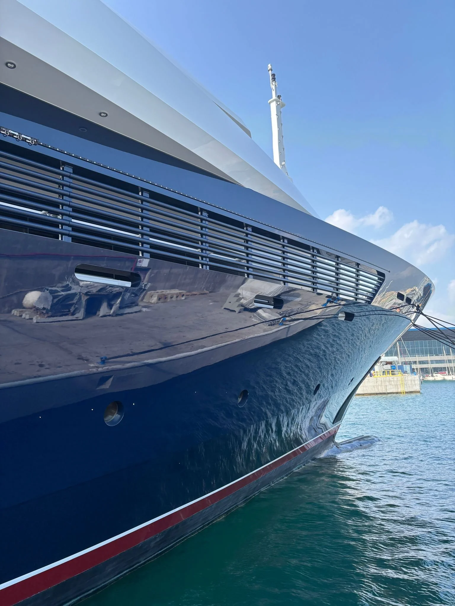 Close-up of the bow of a large luxury yacht docked at a harbor, showing the hull, windows, and the water reflecting the boat.