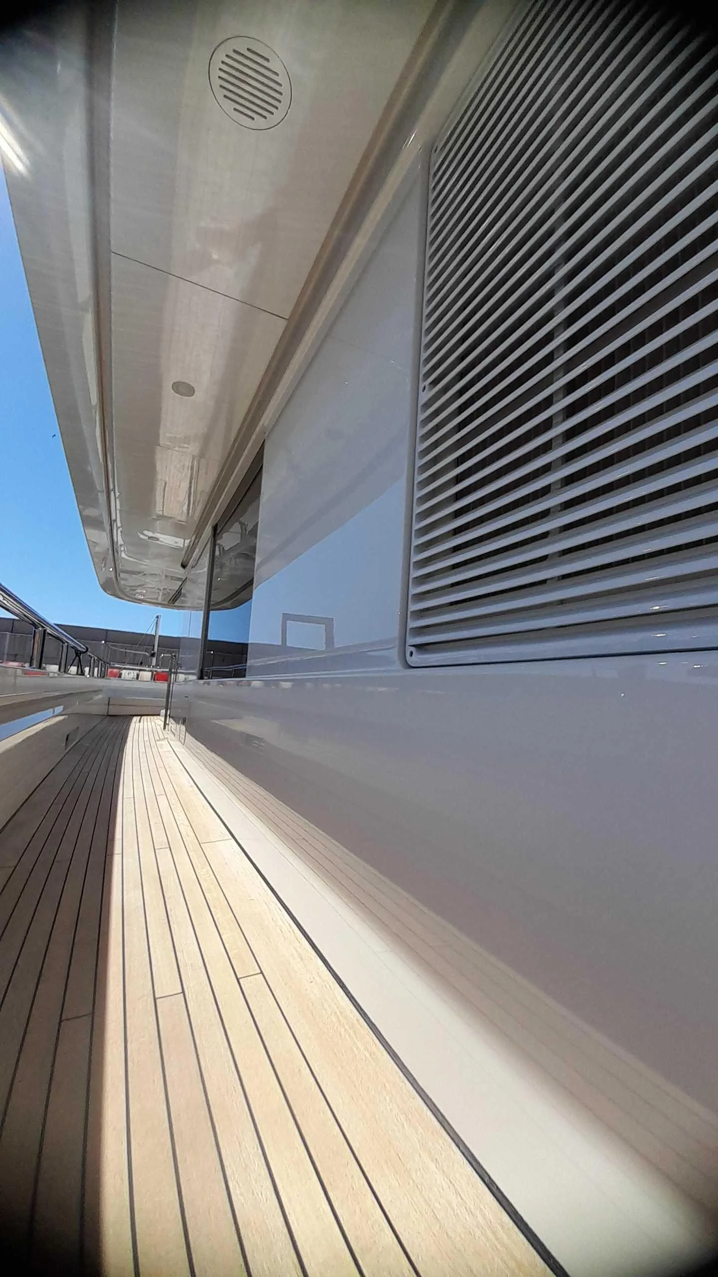 Close-up view of the side of a yacht with a wooden deck and a white exterior wall, showing a large air vent and part of an overhanging roof.