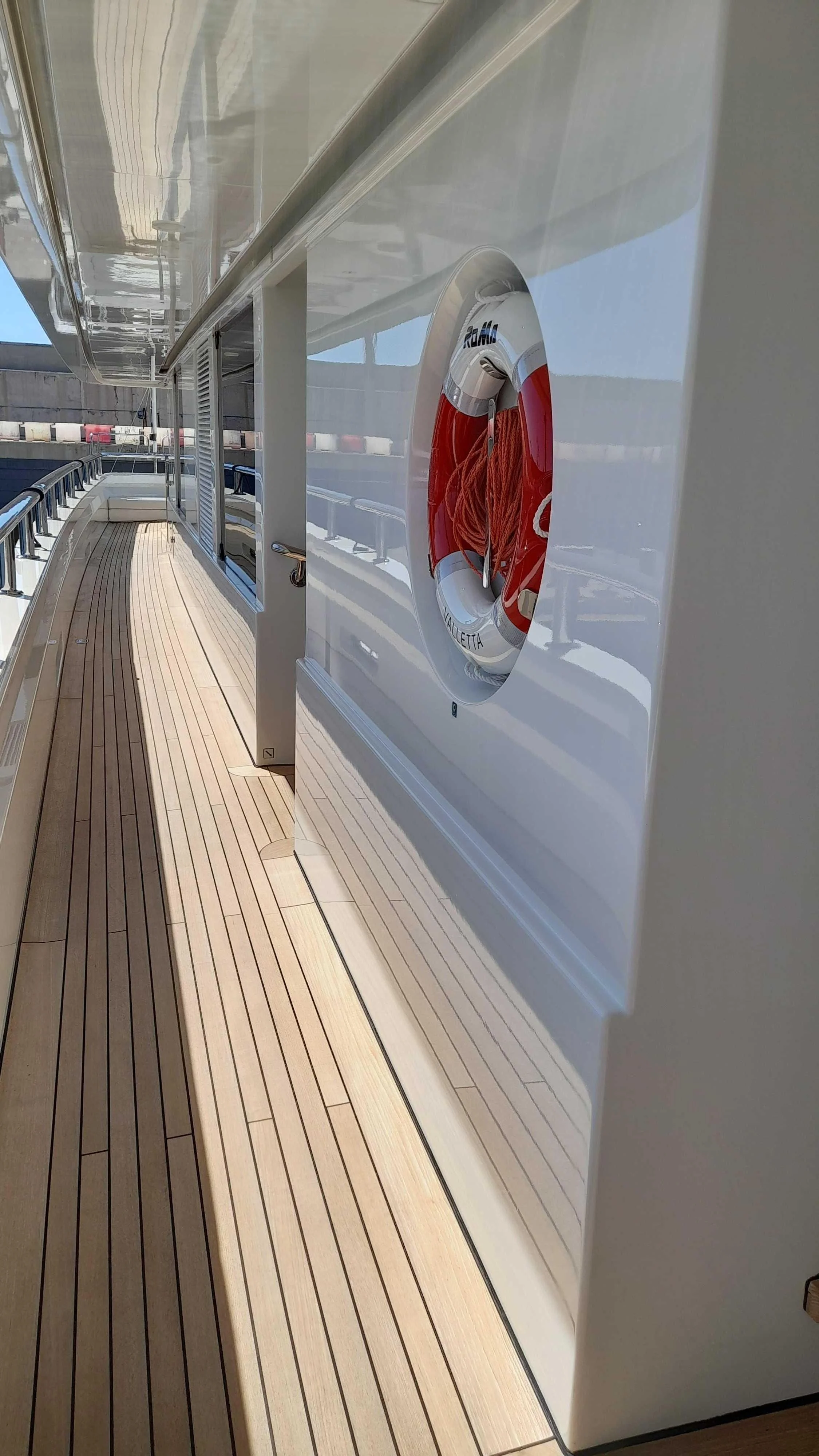 Close-up of a ship's deck with a mounted life preserver containing red rope, overlooking a marina with boat docks in the background.