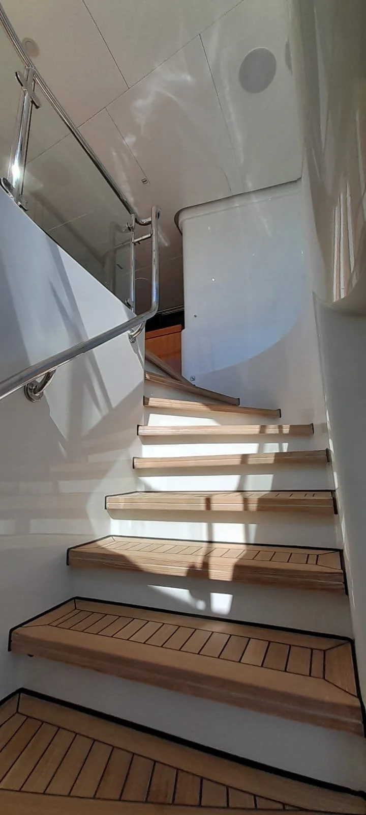 A staircase with wooden steps, a metal handrail, and a white vessel next to a tiled floor and a drain.