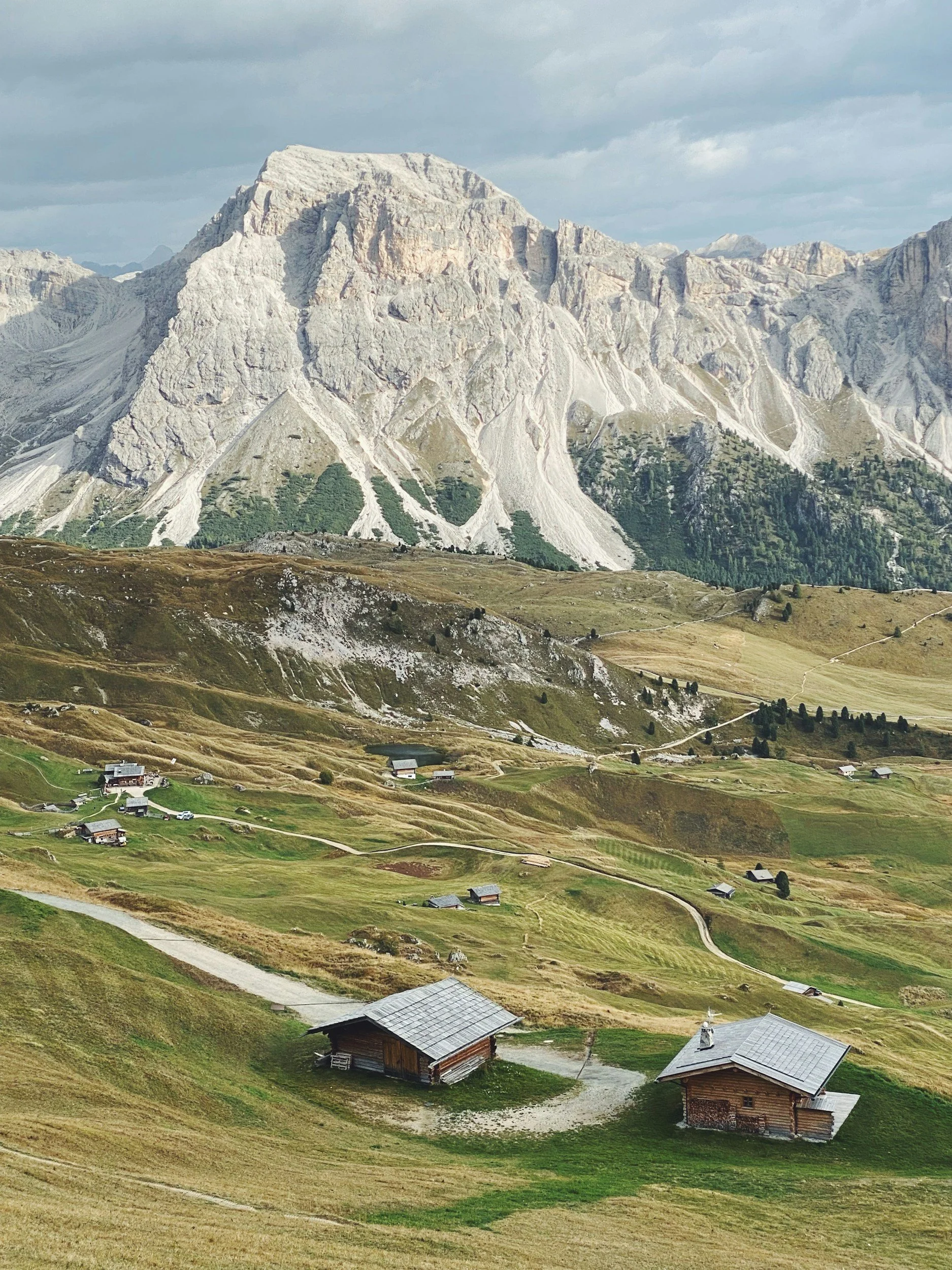 Landscape with a mountain in the background and a grassy hillside with small houses and pathways in the foreground.