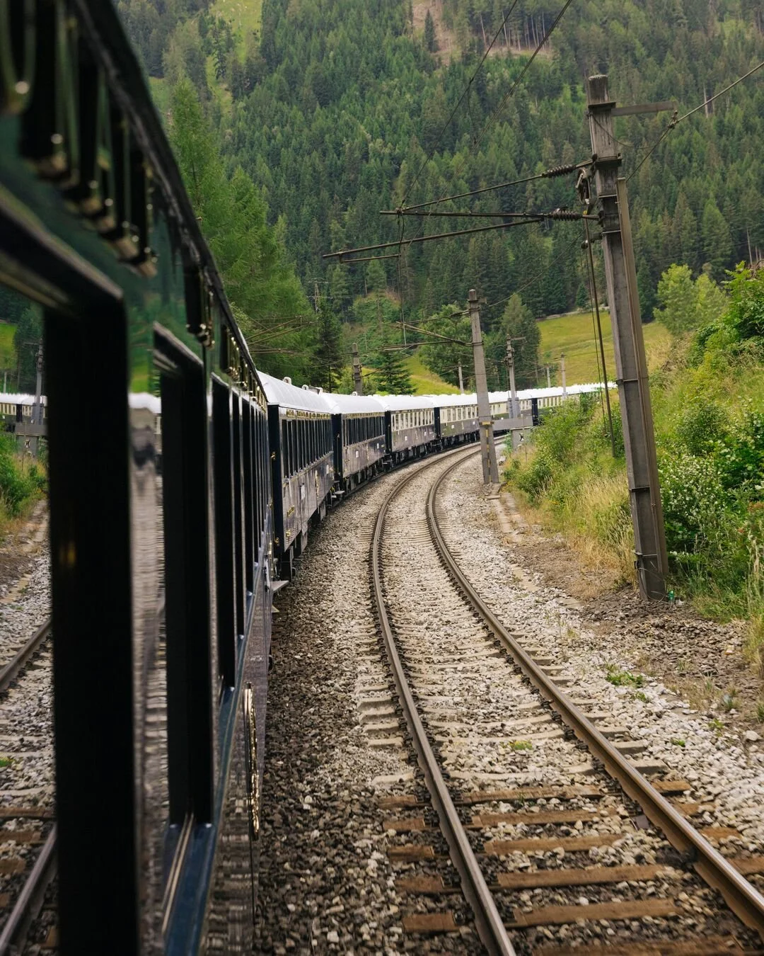A train traveling on curved tracks through a lush green forested mountainous landscape.