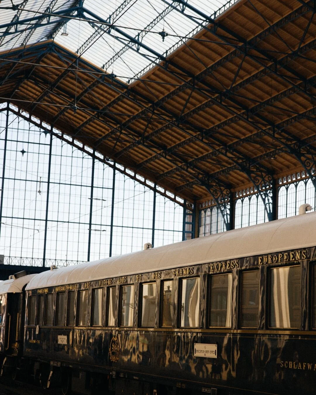 A vintage black and gold train car inside a large train station with a glass and metal ceiling.