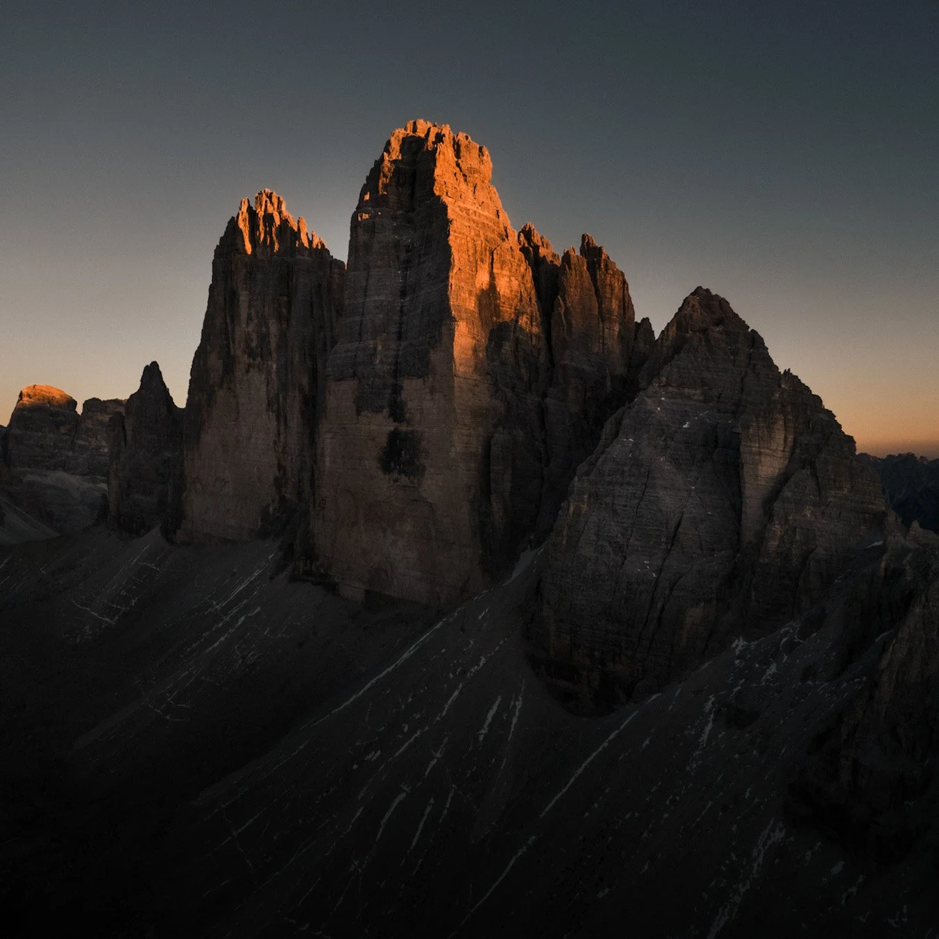 Sunset lighting on rugged mountain peaks of the Dolomites with steep slopes and rocky formations in a remote mountain range.