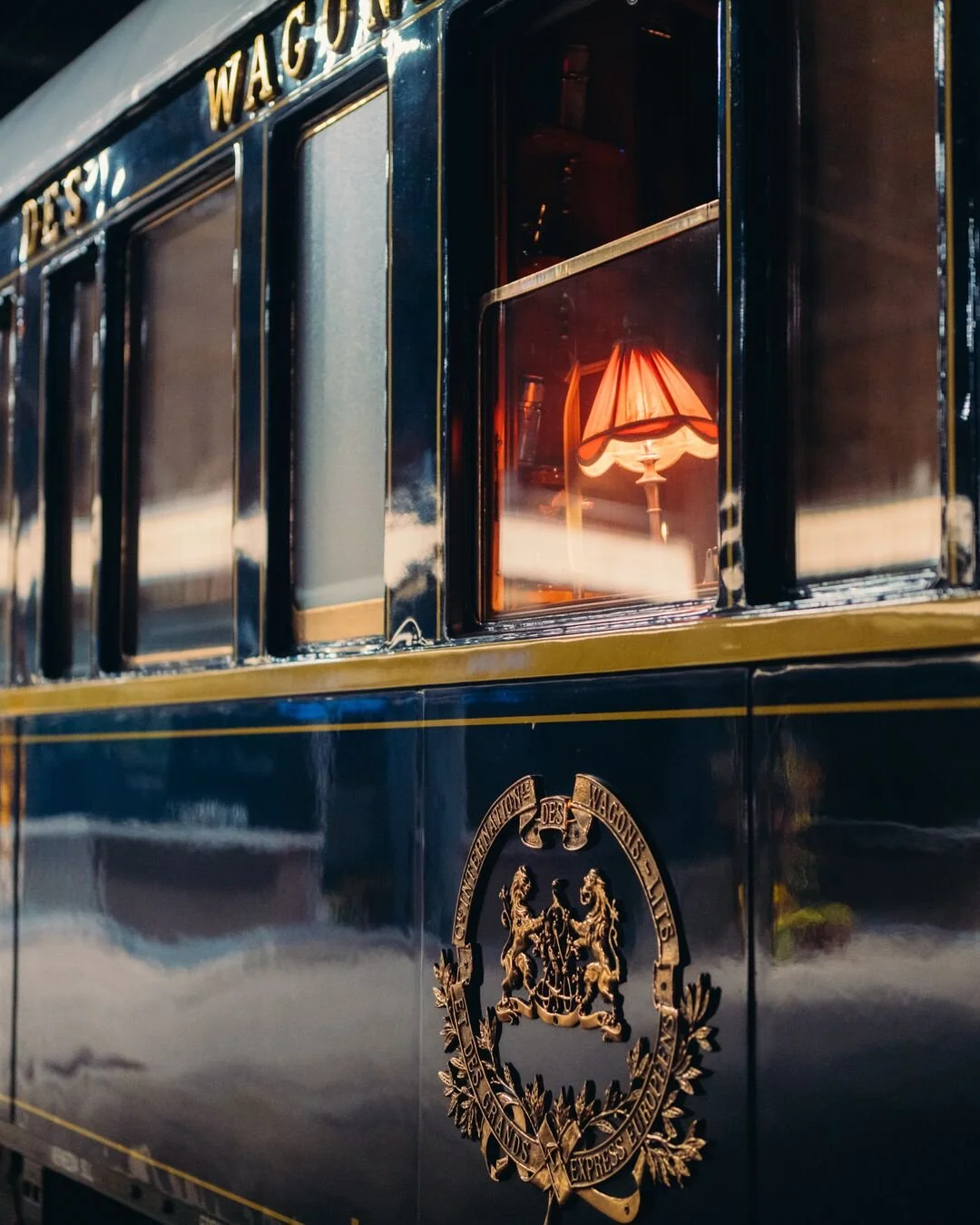 Close-up of a vintage blue wagon with gold trim and a decorative emblem, featuring a lit table lamp inside visible through the window.