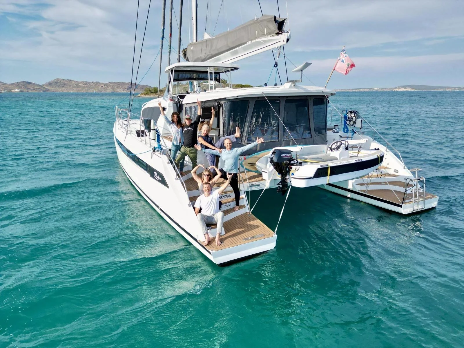 A group of people on a white yacht anchored in turquoise water with a distant landmass and blue sky in the background.